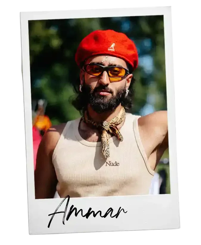 Man met een rood petje, zonnebril en een beige tanktop met het woord 'Nude', buiten op een zonnige dag.