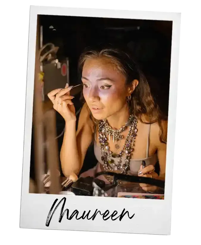 Een vrouw die zich opmaakt met veel sieraden, waaronder kettingen en oorbellen, terwijl ze zich voorbereidt voor een fotoshoot of optreden.