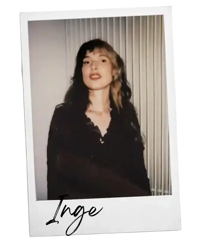 Een foto van een jonge vrouw met lang, gekruld haar, gekleed in een zwarte blouse, lachend voor een lichte achtergrond met verticale strepen. Onderop de foto staat de naam 'Inge' geschreven.