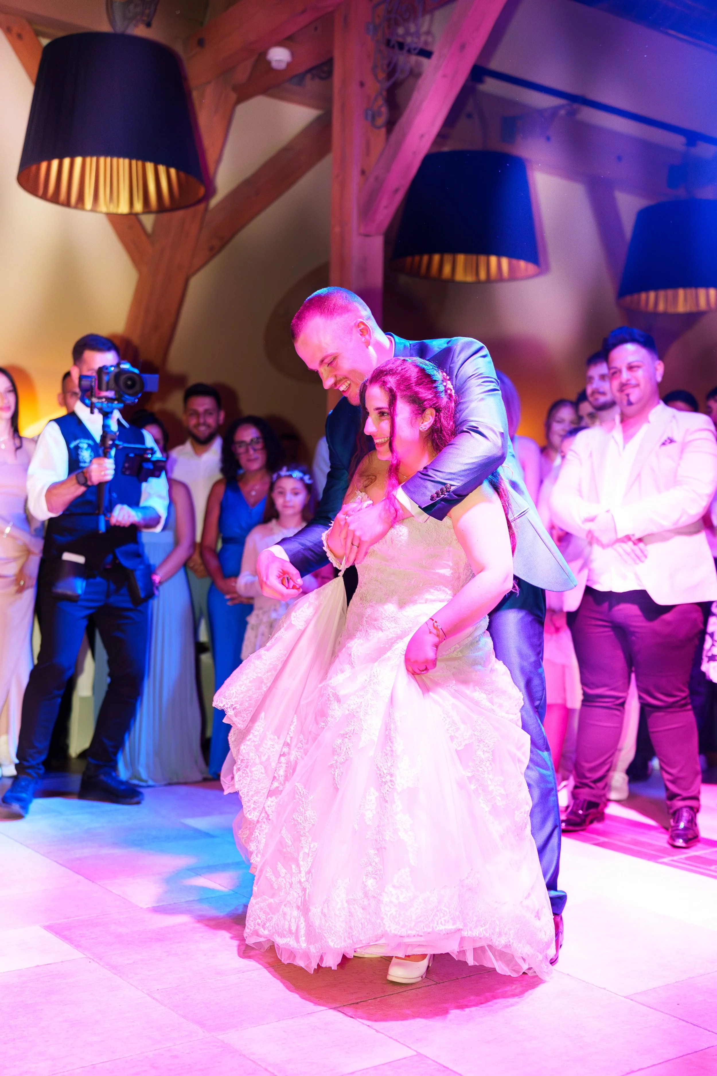 Braut und Bräutigam tanzen auf einer Hochzeitsfeier, umgeben von Freunden und Familienmitgliedern in einem festlichen Raum.