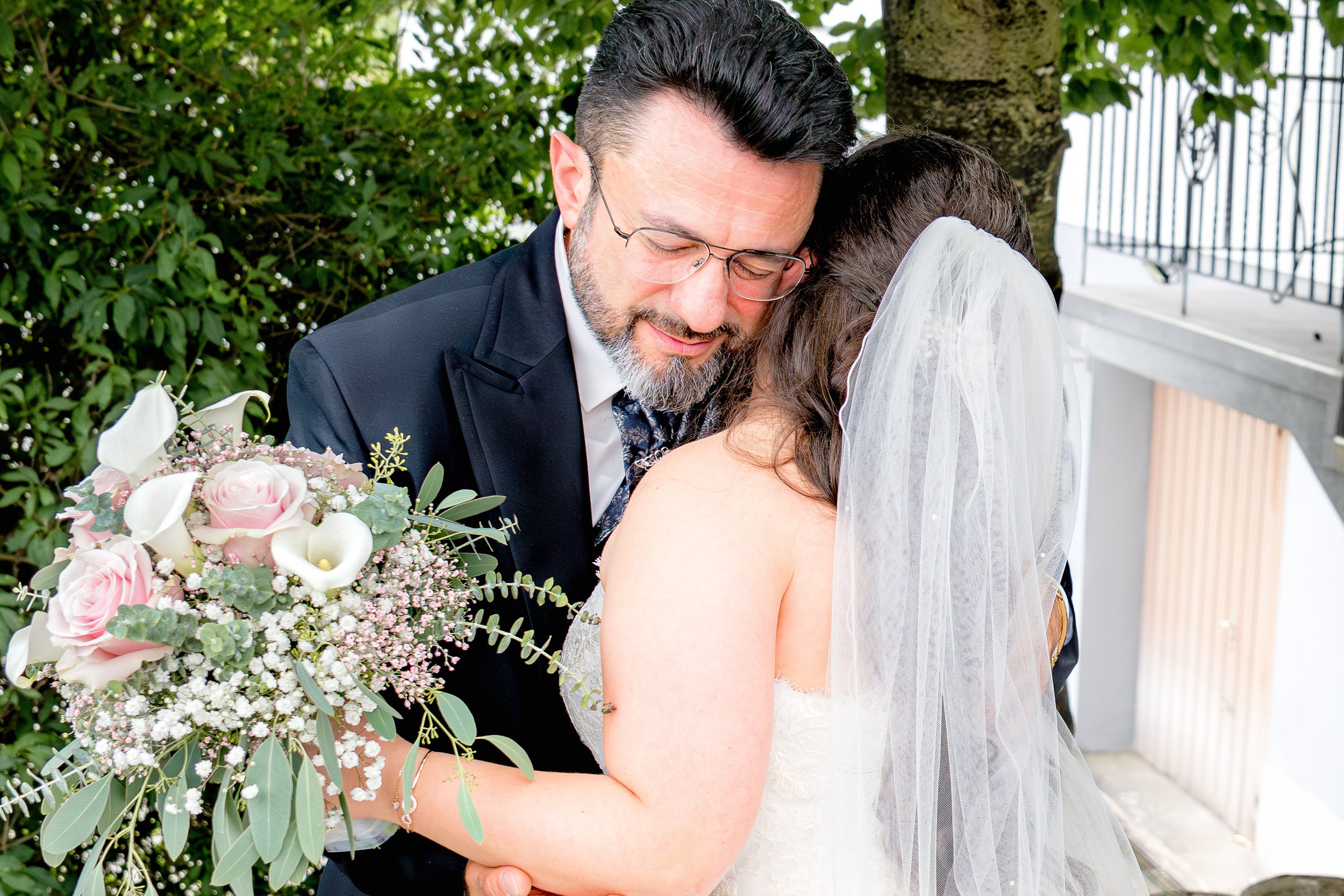 Der Papa der Braut umarmt liebevoll seine Tochter. Sie hält ihren Brautstrauß in der Hand. 