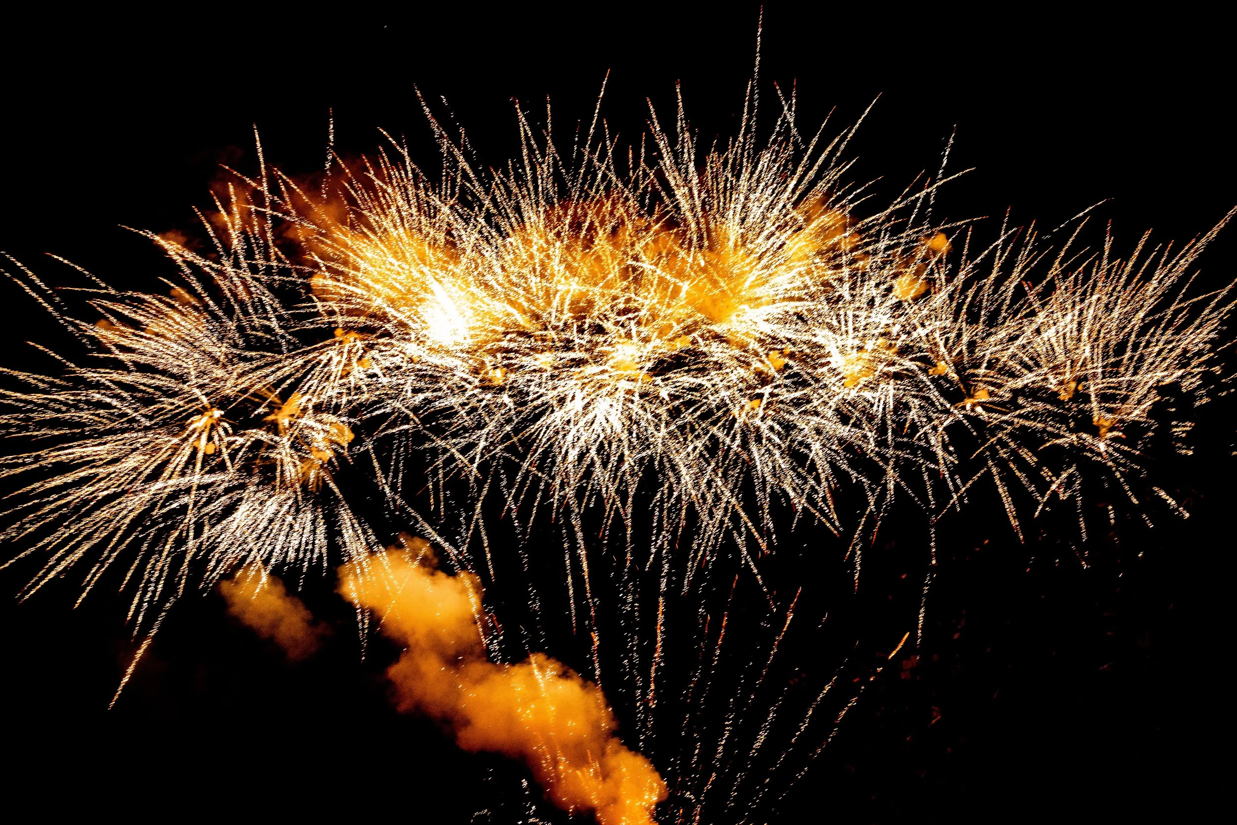 Feuerwerkskörper explodieren am Nachthimmel mit goldenen Funken und Rauch.