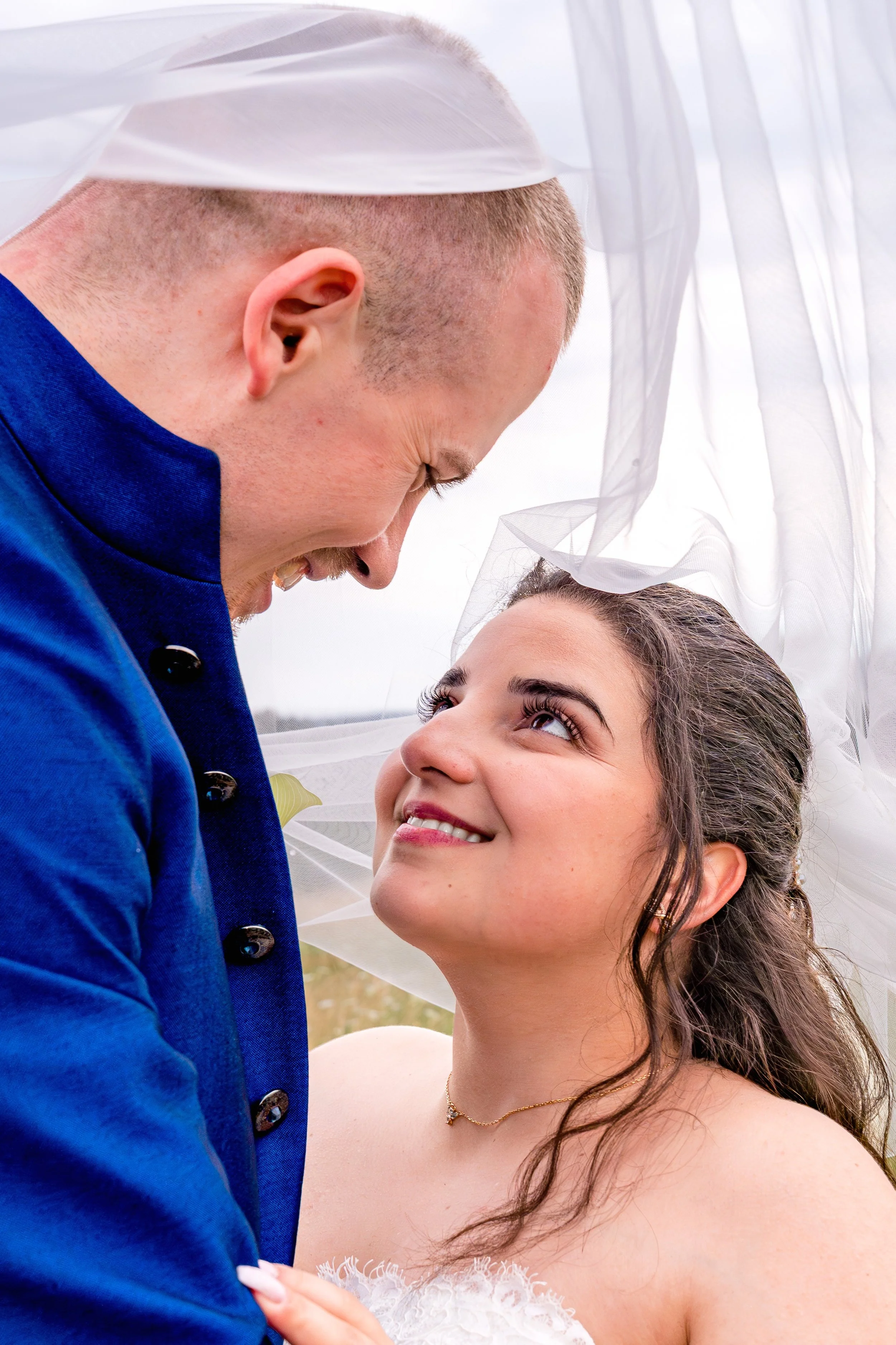 Ein Brautpaar das unter dem Schleier steht und sich liebevoll anschaut. 