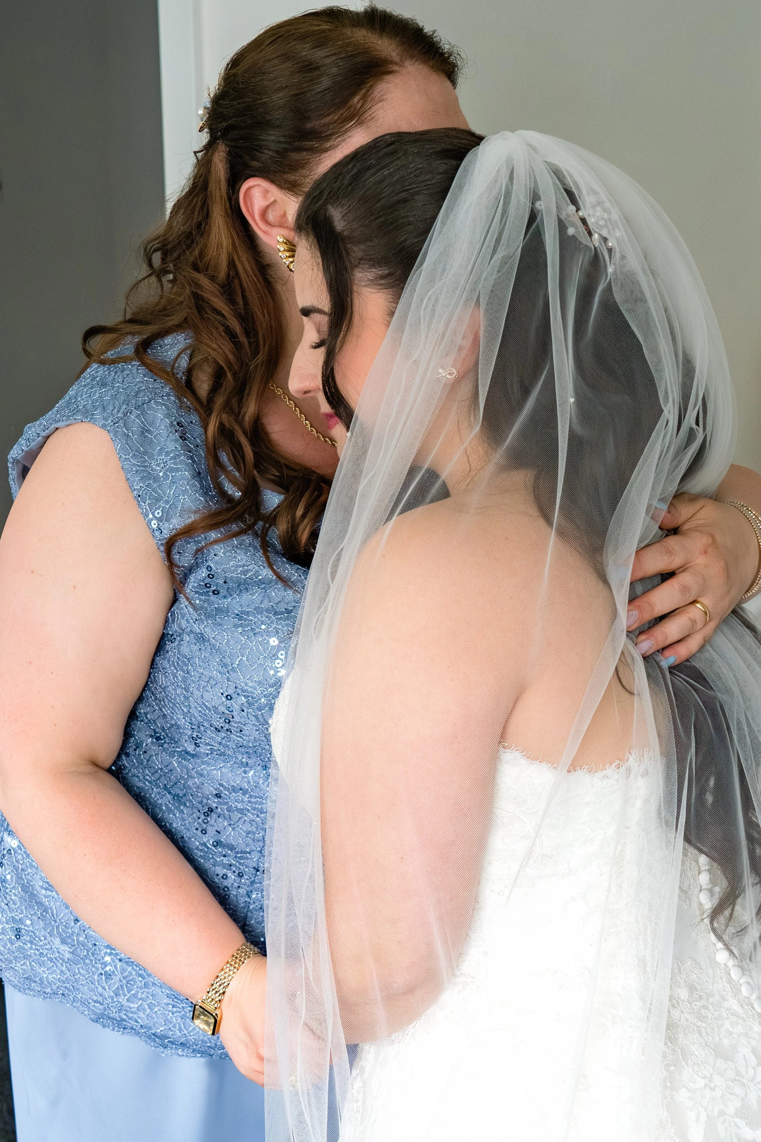 Zwei Frauen, eine Braut in Hochzeitskleid mit Schleier und ihre Mama, die sie umarmt, in einem emotionalen Moment beim Brautstyling im Hotel zur Sonne in Bodelshausen.