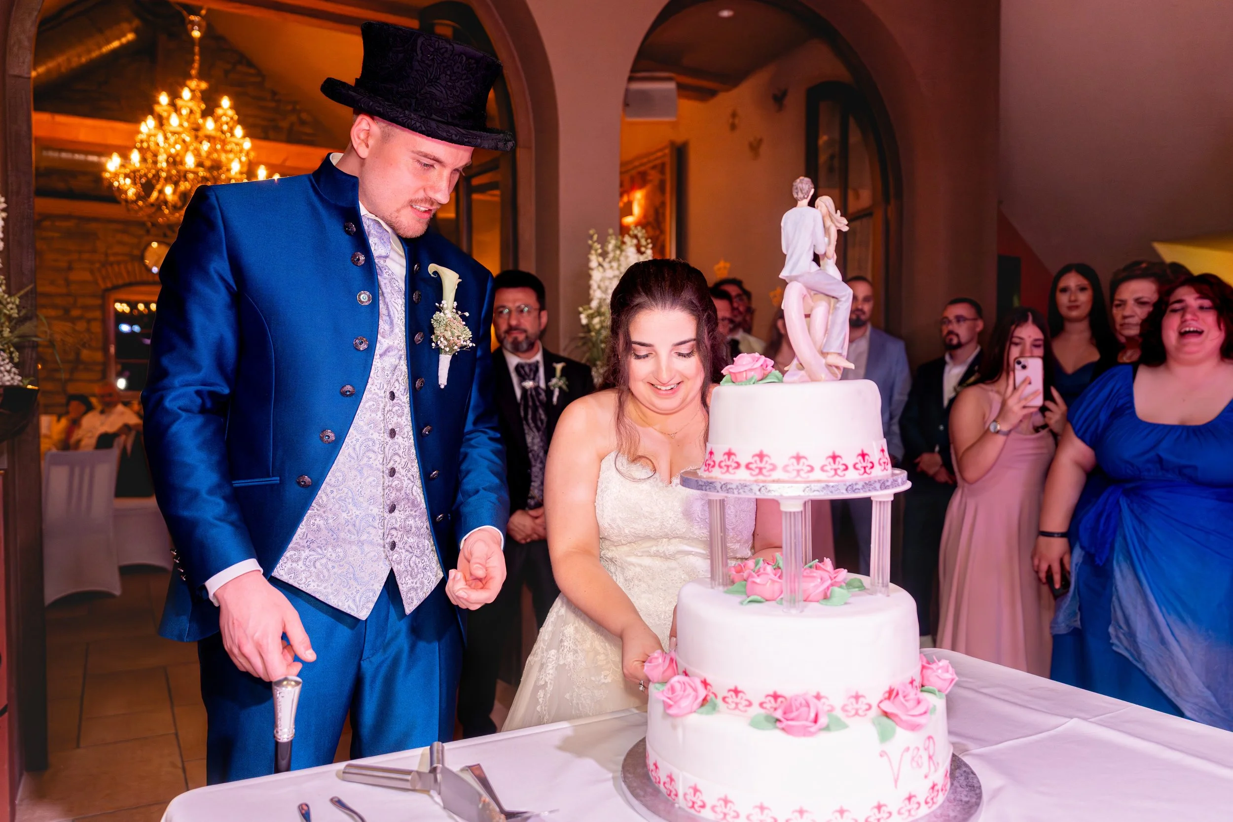 Braut und Bräutigam schneiden die Hochzeitstorte in einem festlichen Raum mit Gästen.