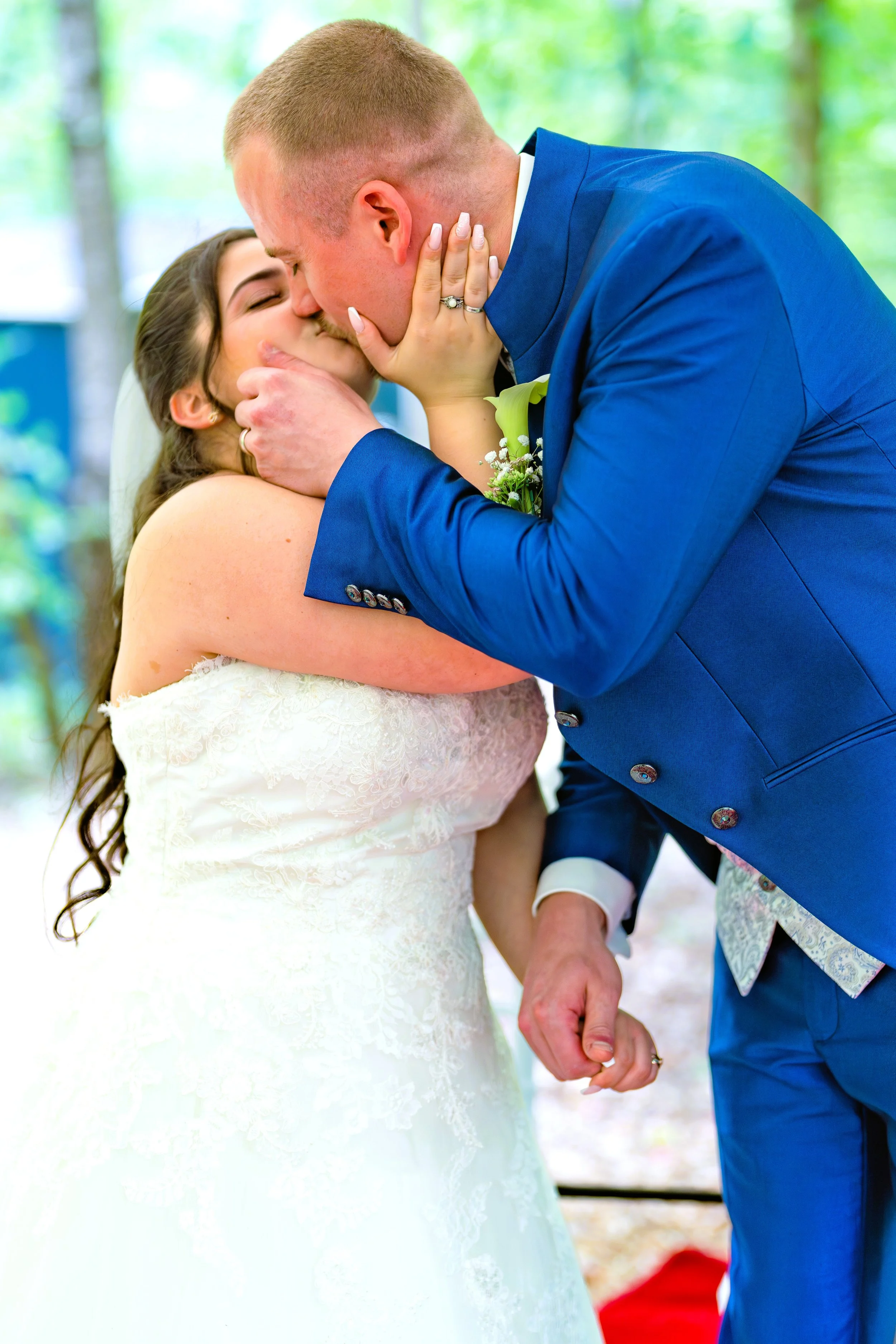 Ein frisch vermähltes Paar bei der Hochzeitszeremonie, sie küssen sich, er trägt einen blauen Anzug, sie trägt ein weißes Hochzeitskleid.
