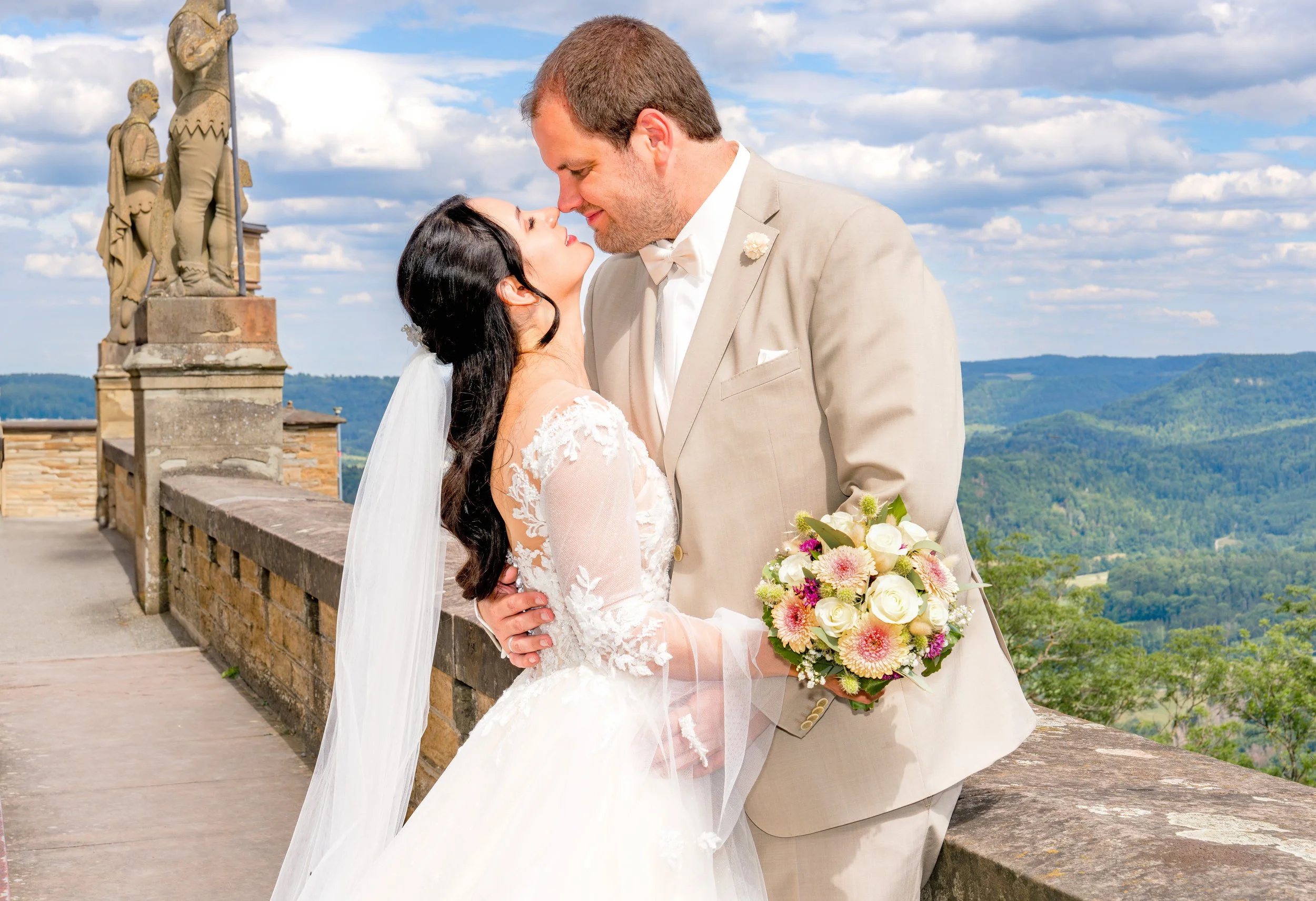 Braut und Bräutigam bei ihrer Hochzeit, die sich auf einer Terrasse mit Blick auf grüne Hügel umarmen.