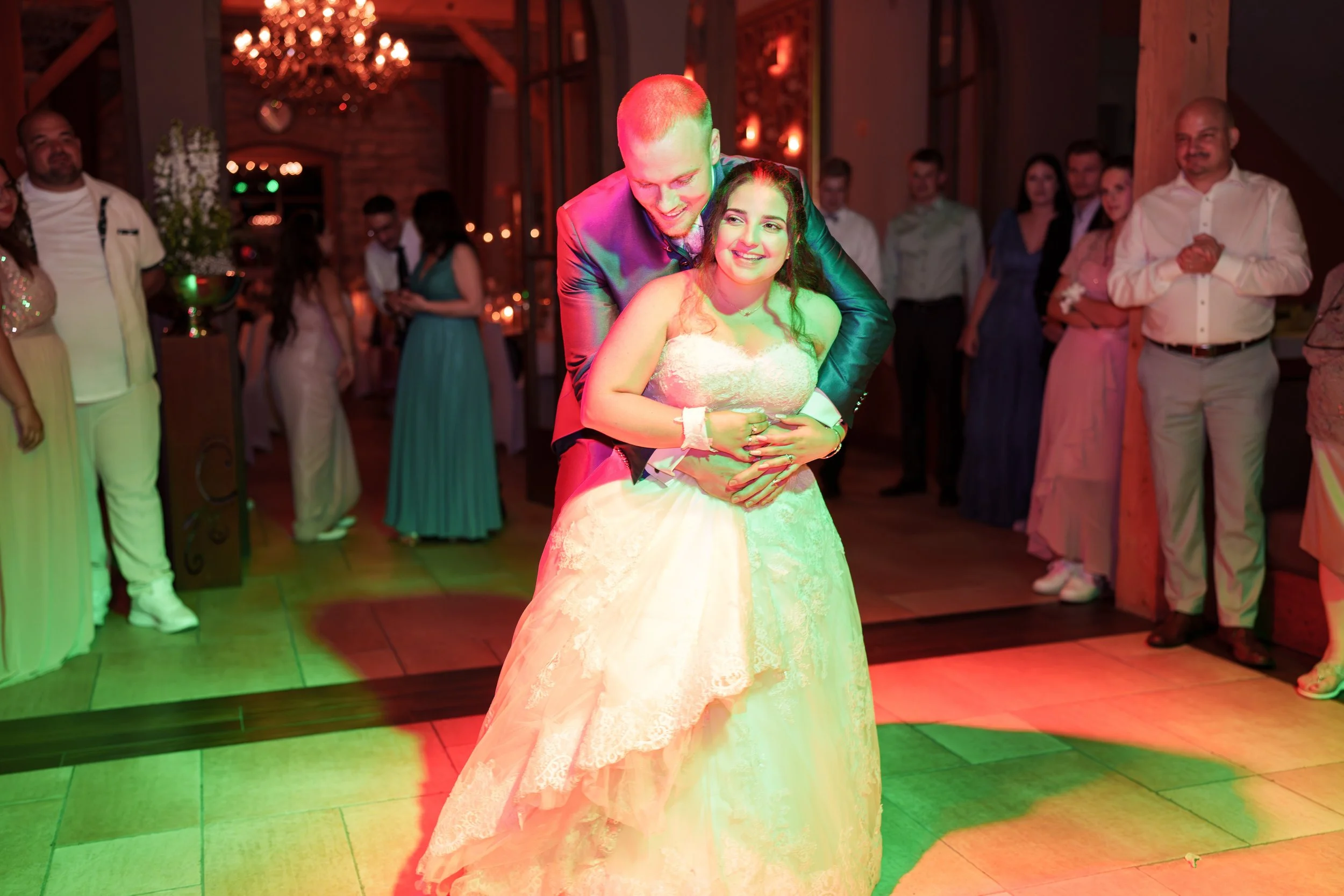 Braut und Bräutigam tanzen bei ihrer Hochzeit, umgeben von Gästen in einer festlich dekorierten Location.
