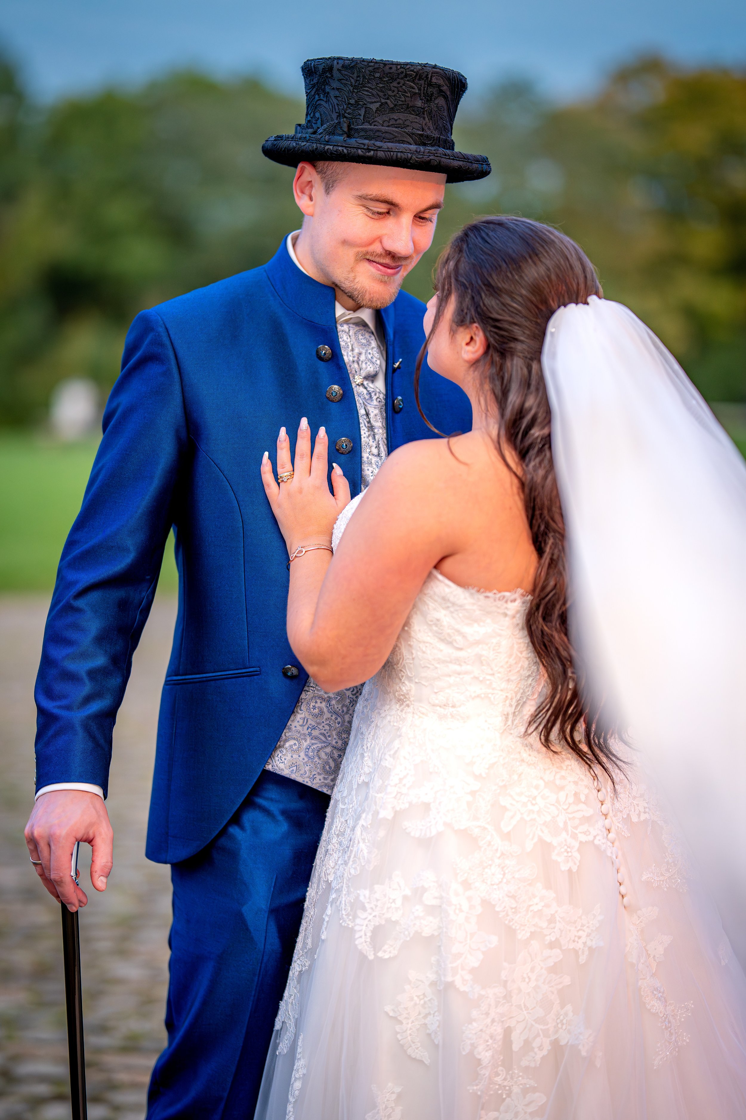 Ein Brautpaar bei der Hochzeit, das sich liebevoll anlächelt, im Freien mit grünem Hintergrund.