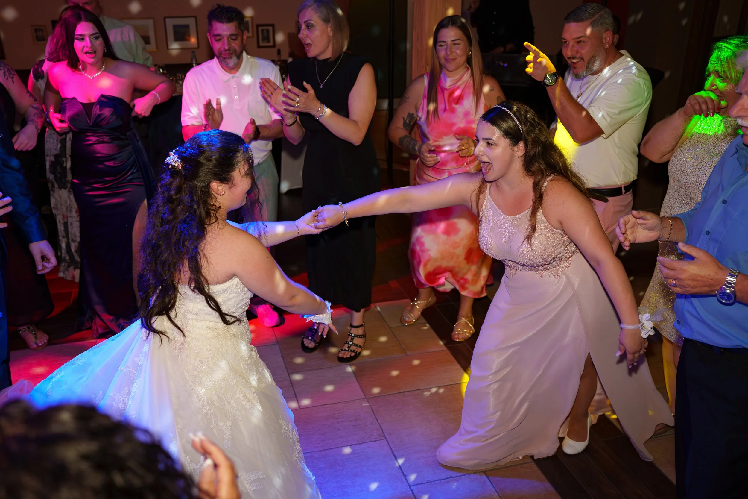 Menschen tanzen und feiern bei einer Hochzeit im Ballsaal, die Braut ist mit einer anderen Frau auf der Tanzfläche, umgeben von Freunden und Familie.