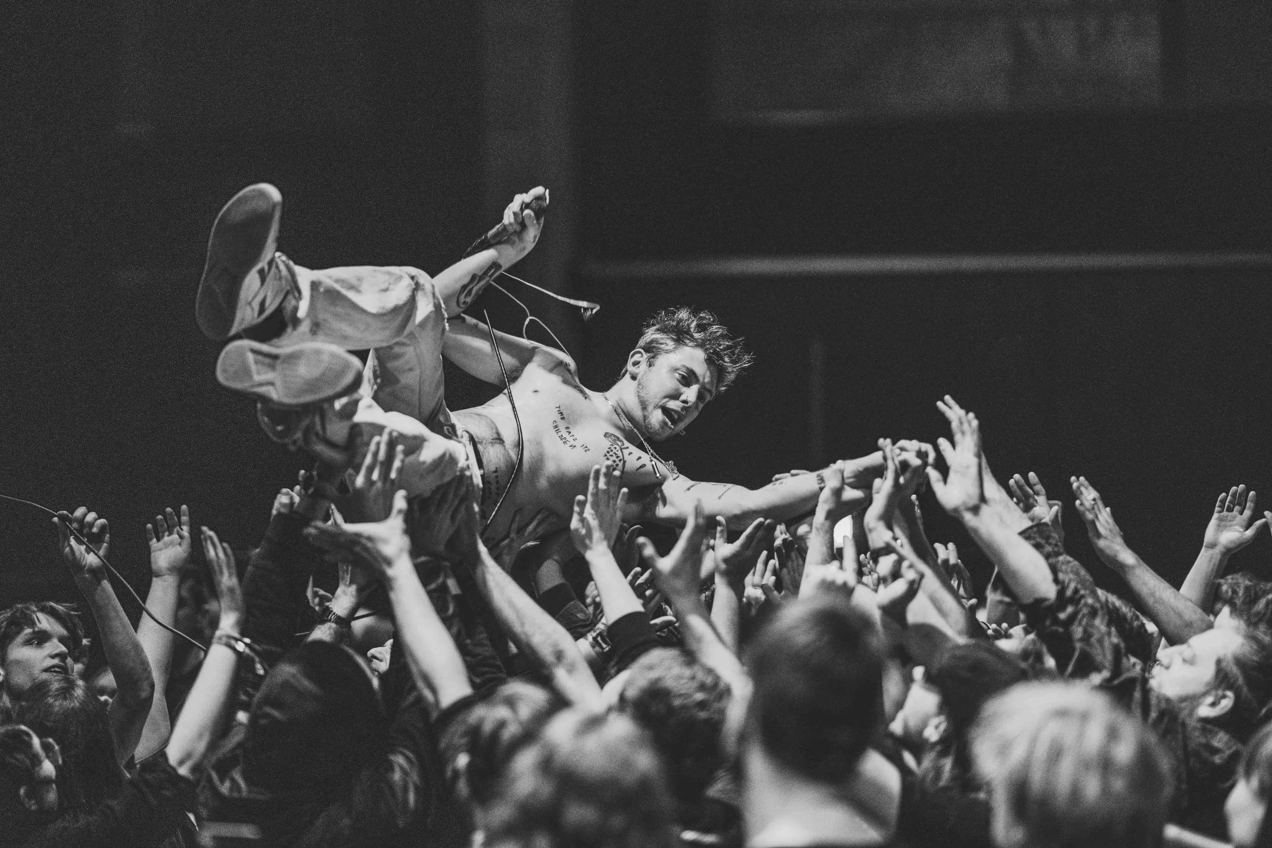 A shirtless male Sam Matlock of Wargasm is crowd surfing on a sea of hands during a concert, with a lively expression.