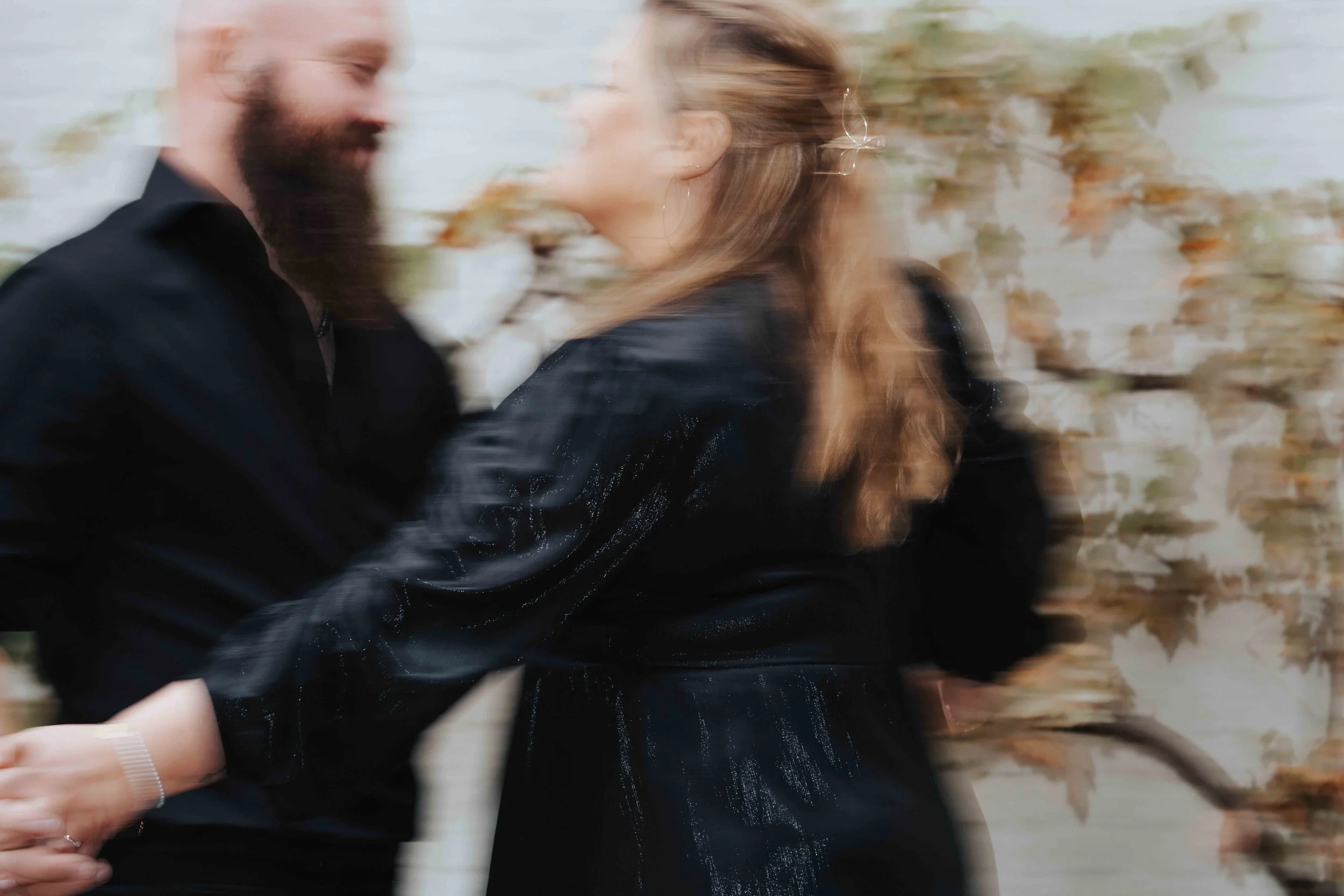 A couple is smiling and running together outdoors among autumn leaves, with motion blur.