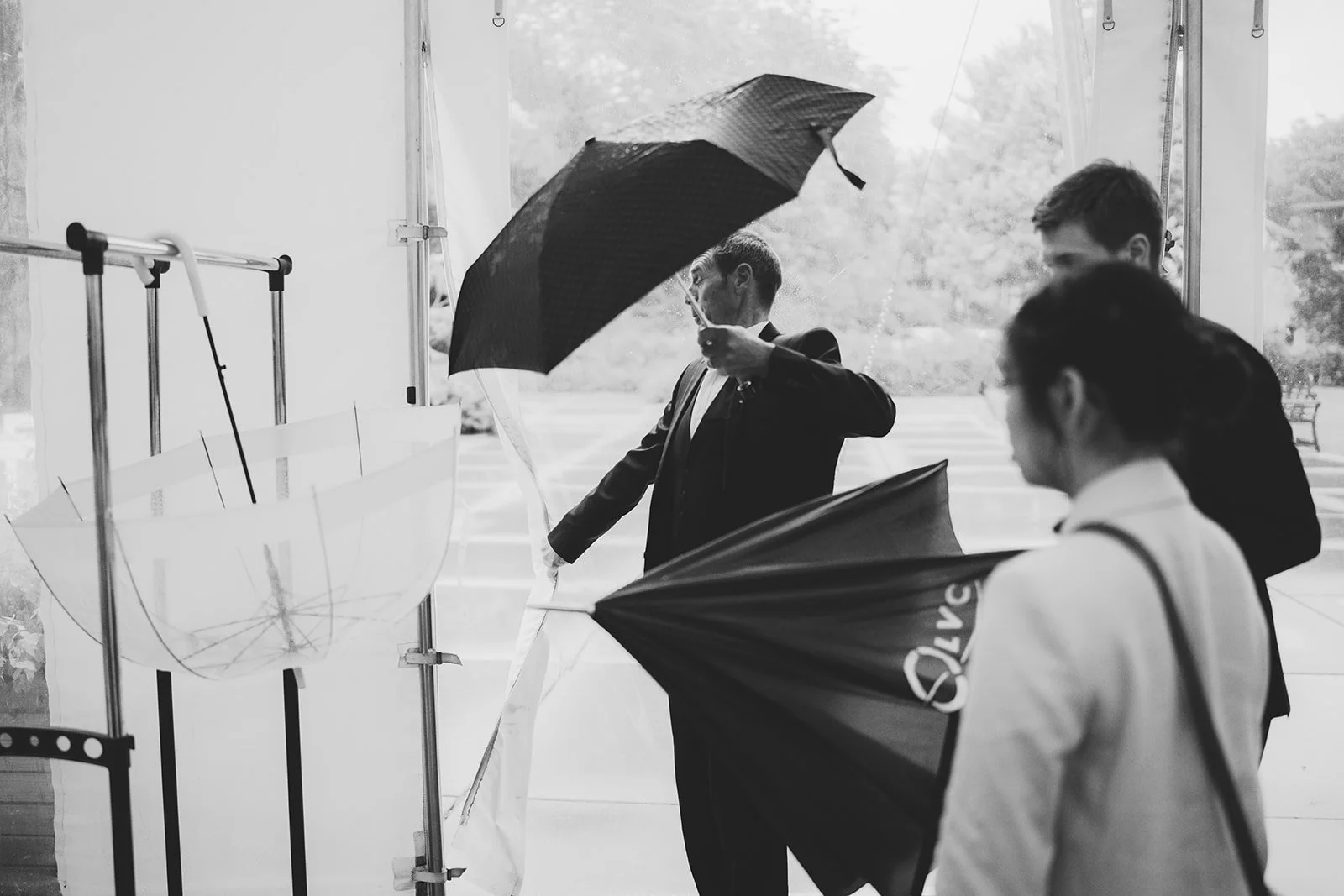 A group of people holding umbrellas, standing near a window with a rainy outdoor scene.