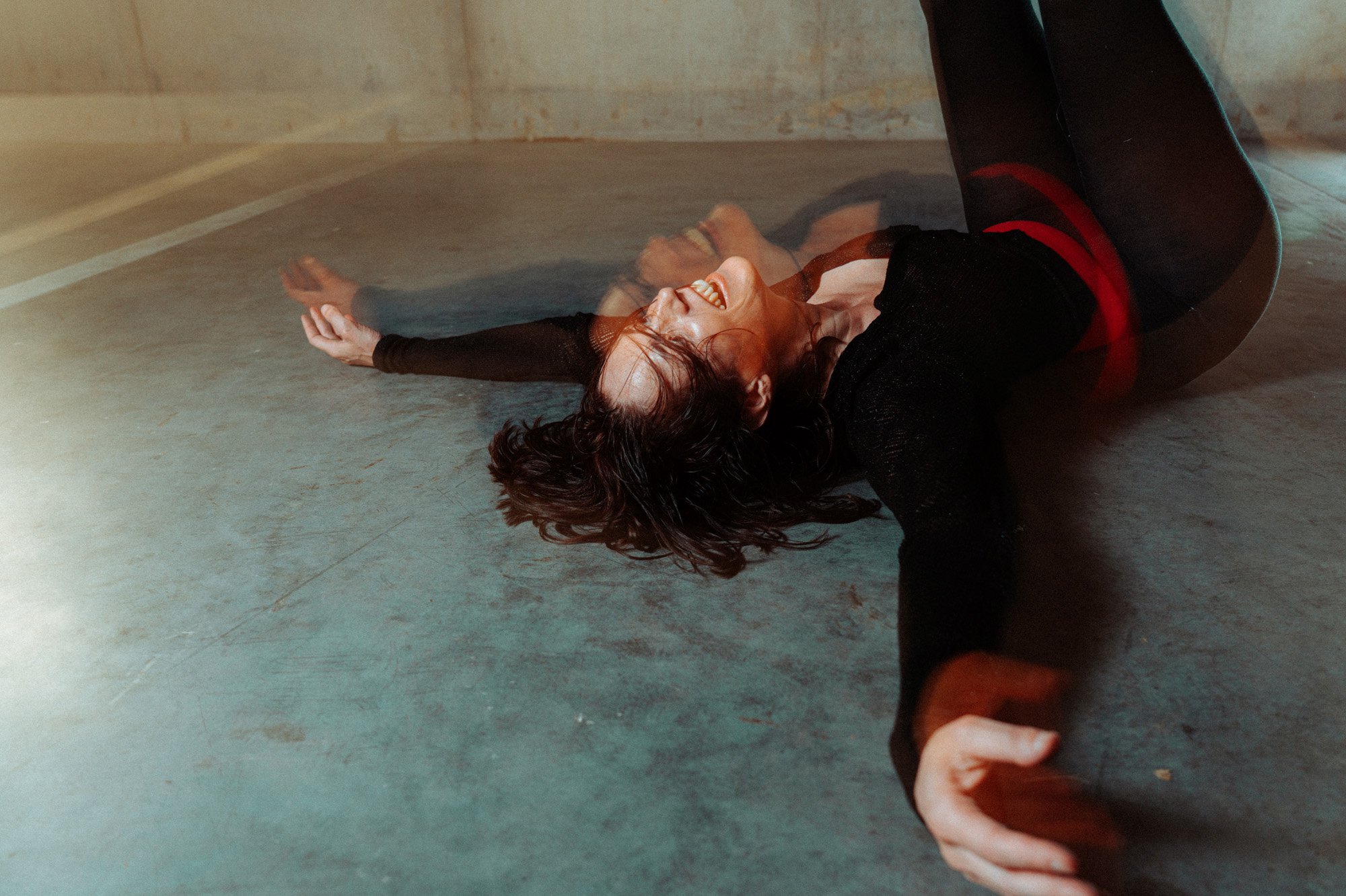 Woman lying on the floor, laughing, with arms extended and head tilted back.