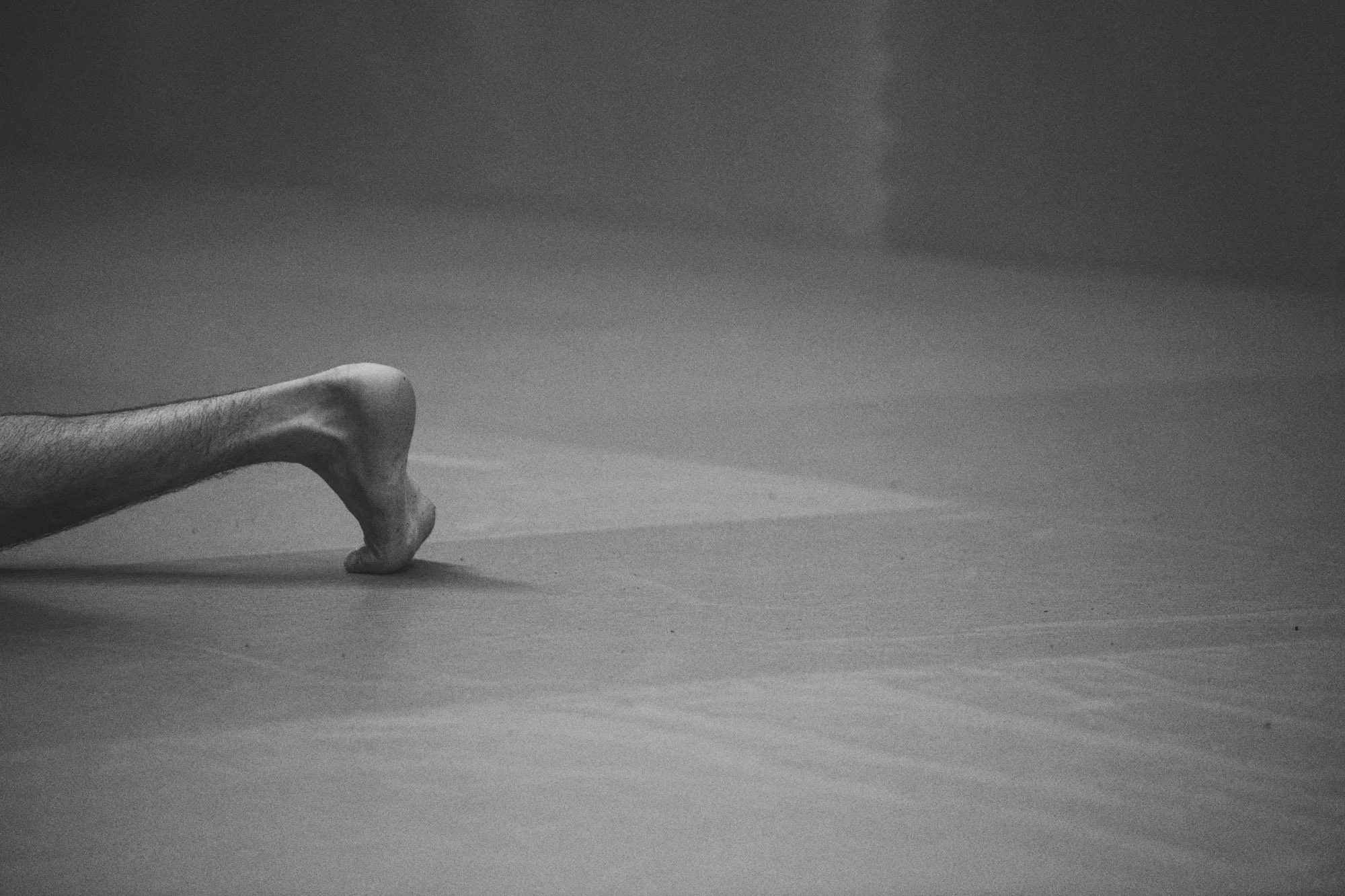 Black and white photo of a person's leg and foot in a push-up position on a smooth surface, with the focus on the foot and the background slightly blurred.