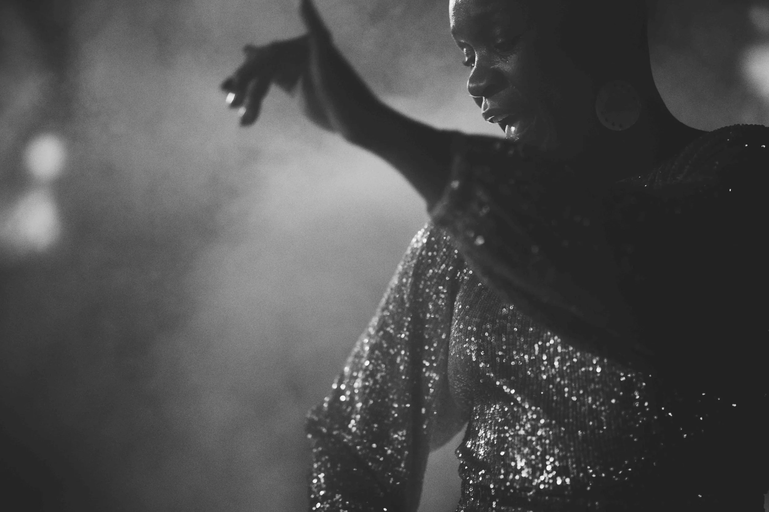 Black and white photo of a woman in a sparkly dress, looking down with her arm raised, earring visible, side profile.