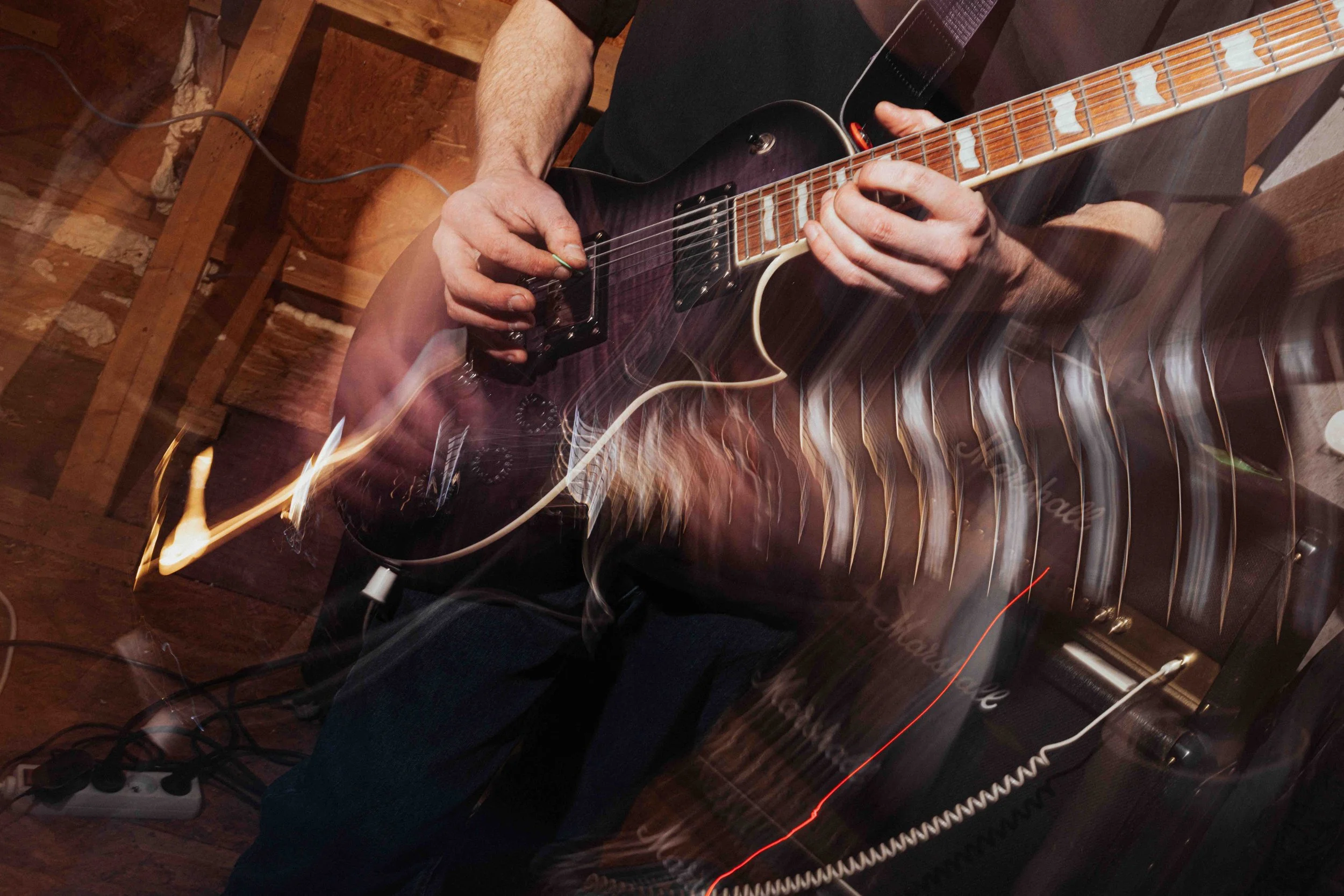 A person playing an electric guitar in a dimly lit room, with motion blur and light streaks.