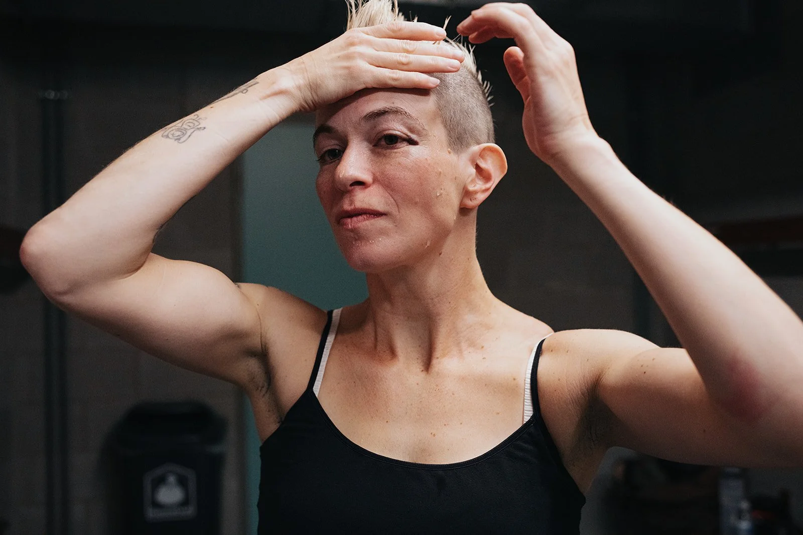 Woman with short hair adjusting her head and checking for a black eye in a gym setting.