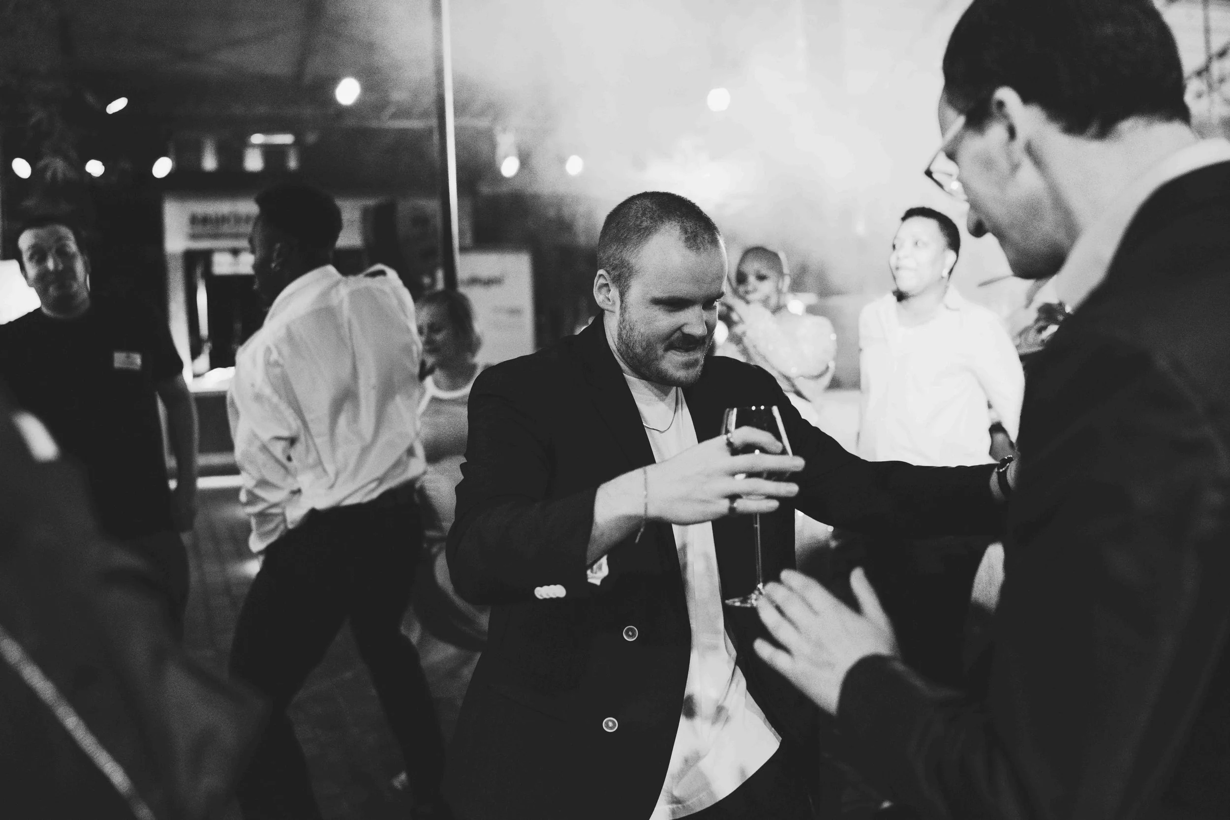 People dancing and socializing at a party, with one person in the center holding a wine glass, in black and white.