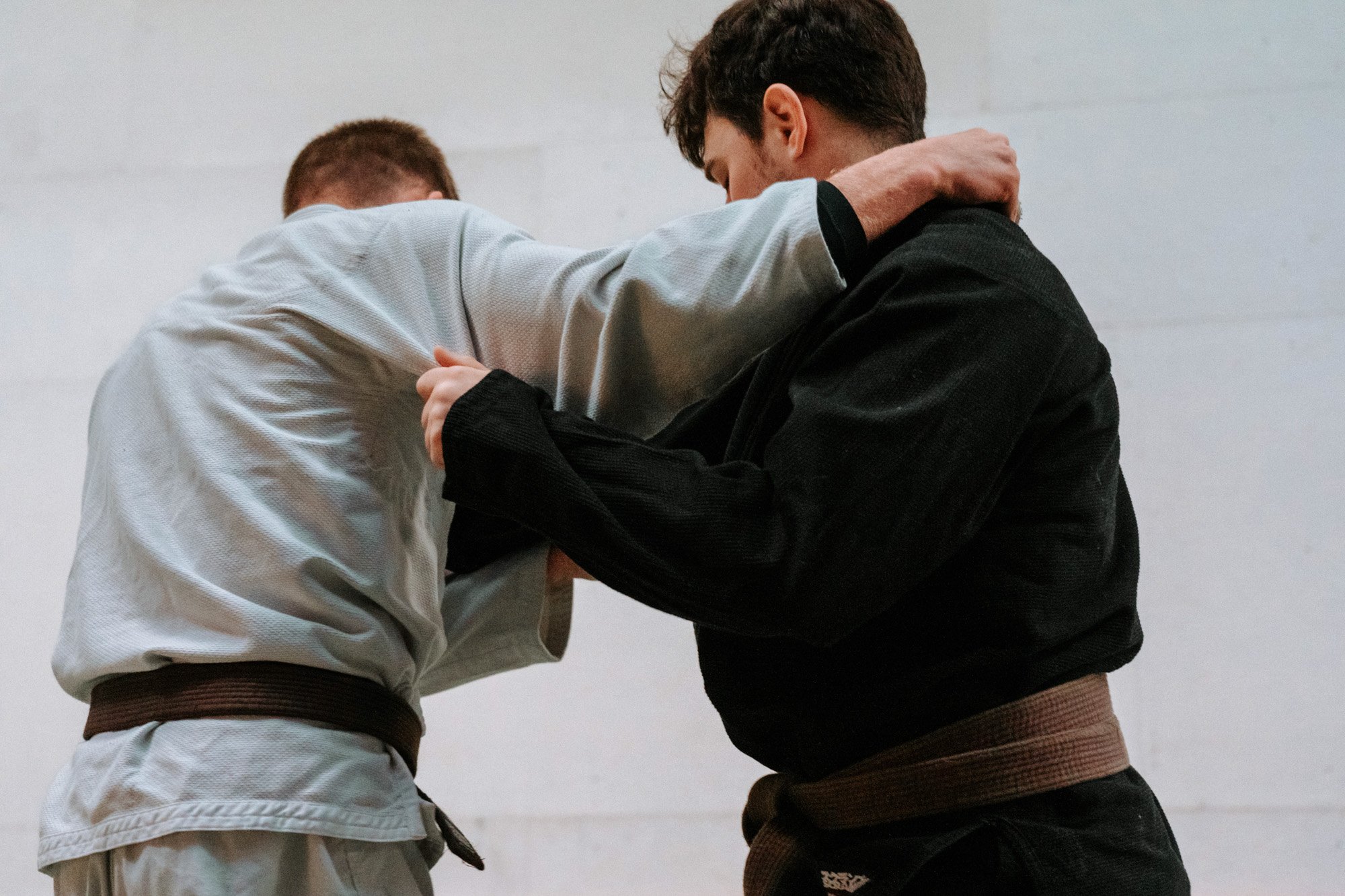 Two men practicing Brazilian Jiu-Jitsu, wearing gi uniforms, engaged in a grappling hold, with one in a black gi and the other in a white gi.