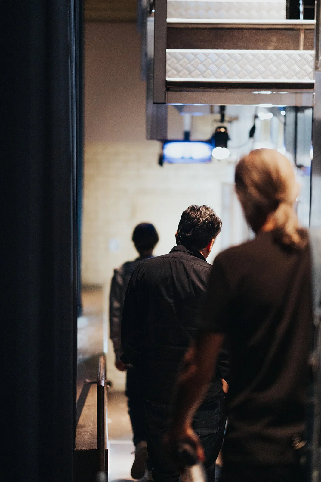 People standing in line indoors, waiting to go upstairs on a staircase.