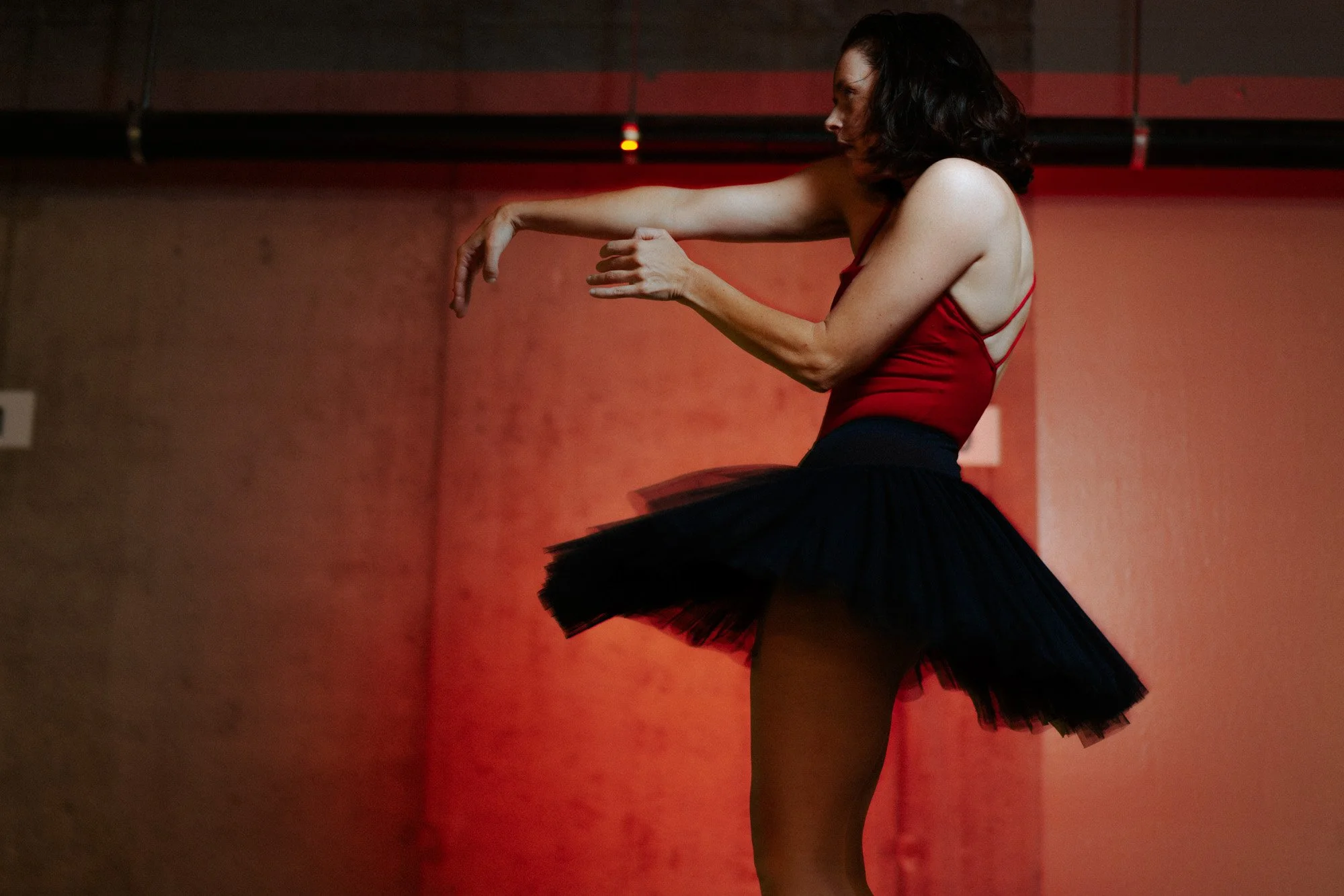 A woman dressed in a red top and black tutu dancing in a parking garage setting with red lighting.