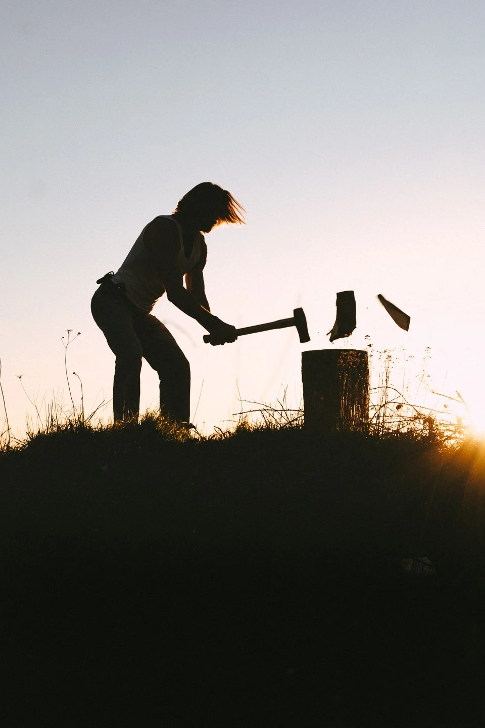 Silhouette of a person chopping a tree stump at sunset