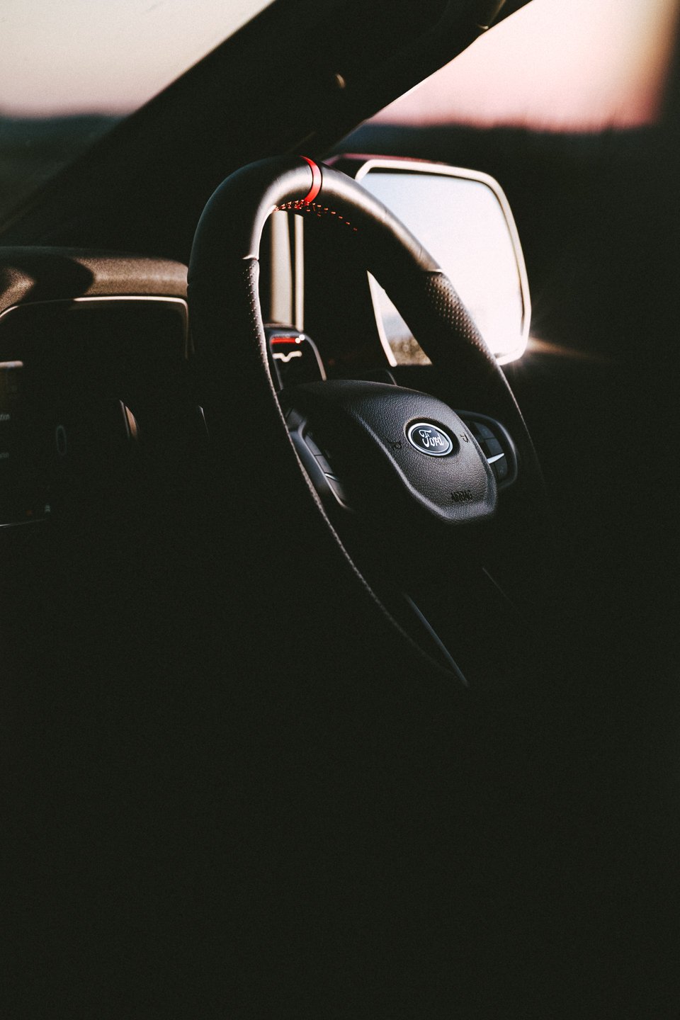 Close-up of a car interior showing a Ford steering wheel and dashboard with a digital display, in dim lighting.