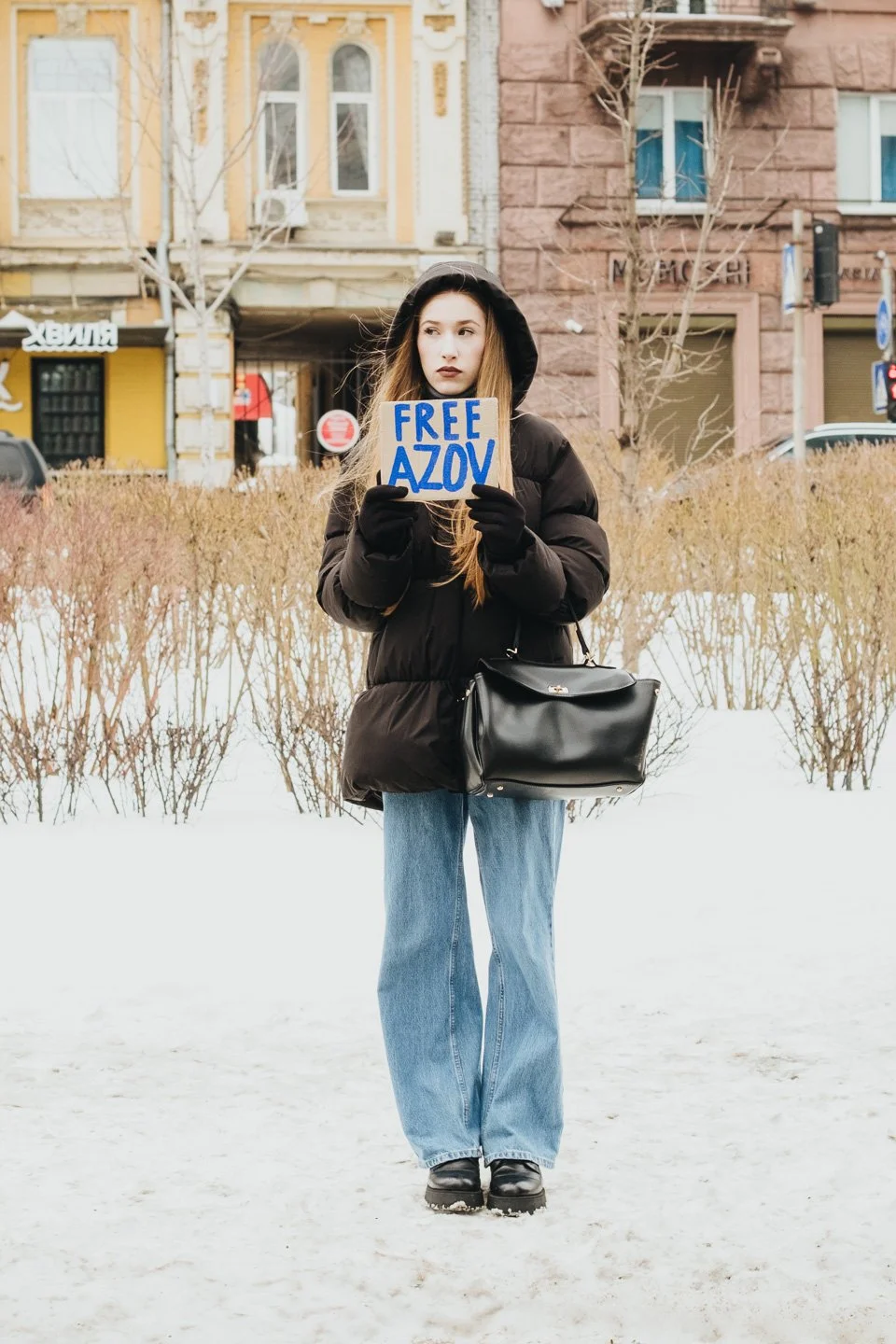 A woman standing in the snow holding a sign that says 'FREE AZOV.'