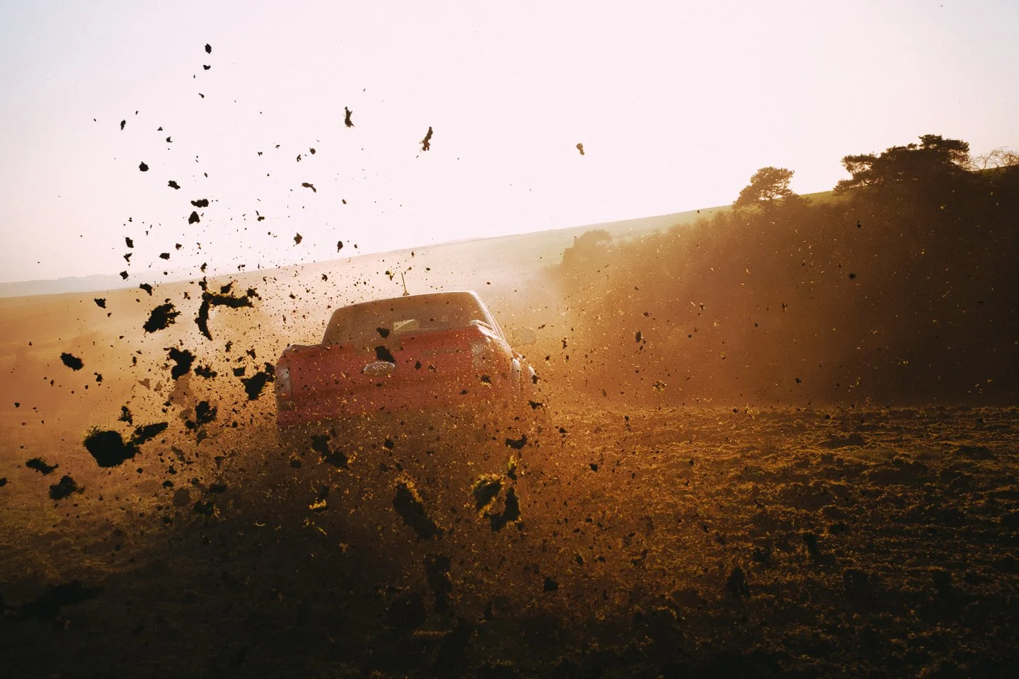 A red pickup truck driving fast on a dirt road, kicking up dust and dirt with dust particles flying in the air during sunset.
