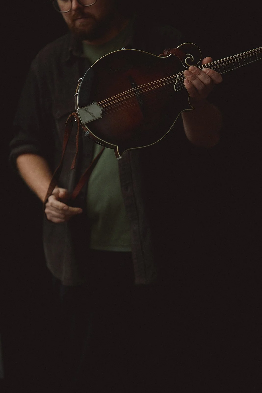 A man holding a mandolin in a dark setting.