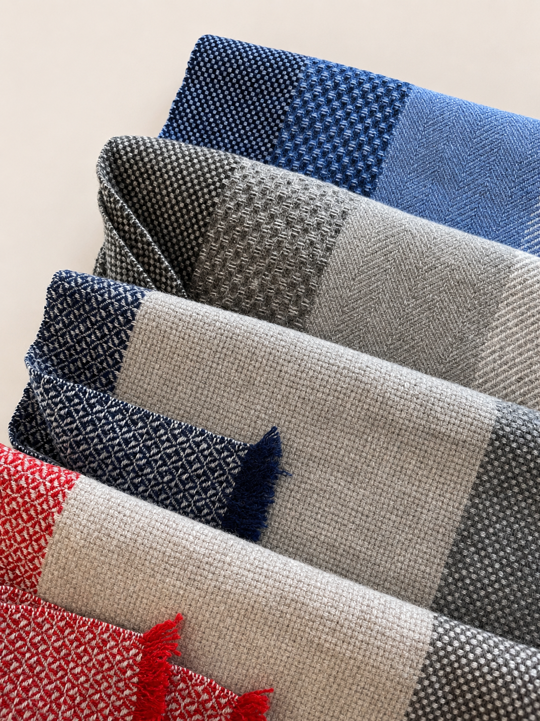 Une pile de tissus ou de foulards avec différents motifs en couleurs rouge, blanc, noir, gris, bleu et beige.