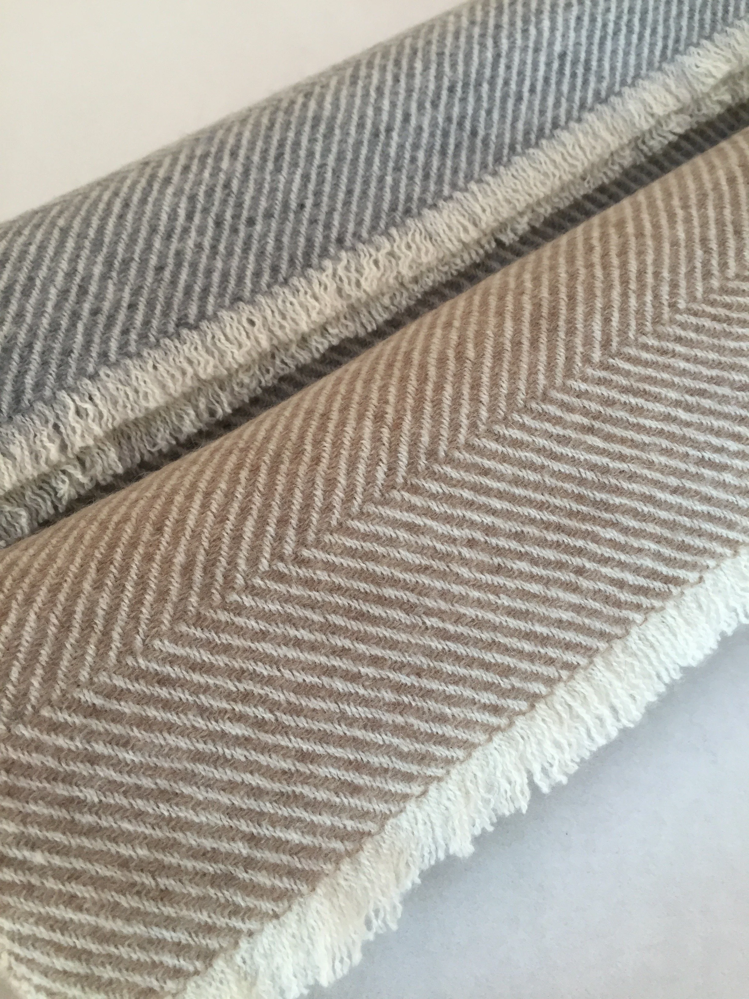 Un tissu en laine à rayures diagonales de teintes gris clair, beige et marron, posé sur un fond blanc.