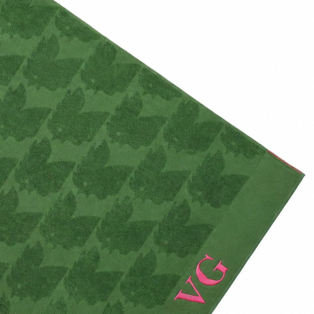 Un tapis de couleur verte avec des motifs de fleurs et de feuilles, et les lettres 'VG' en rose sur un coin.