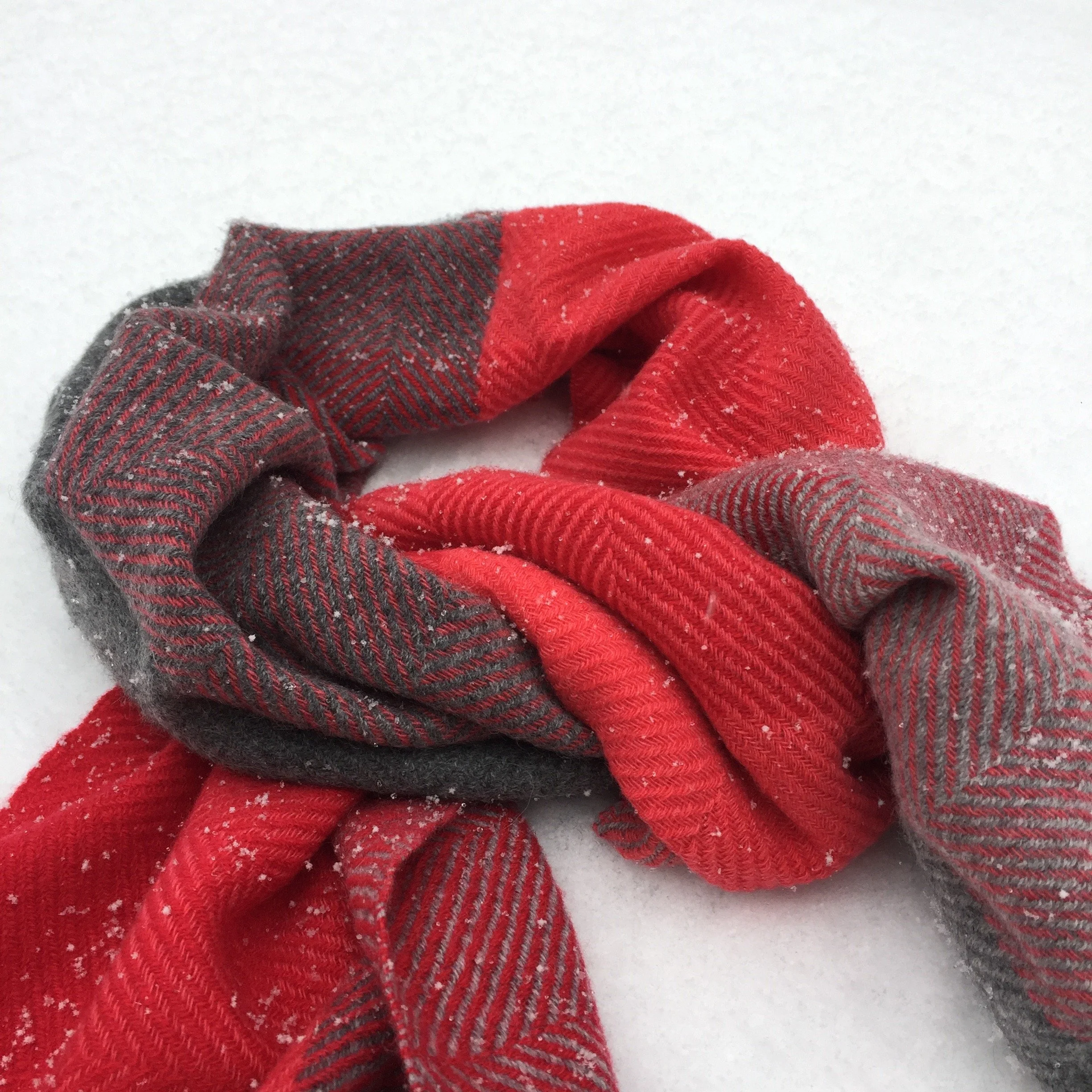 Les mains portent des gants rouges et gris à carreaux, dans la neige.