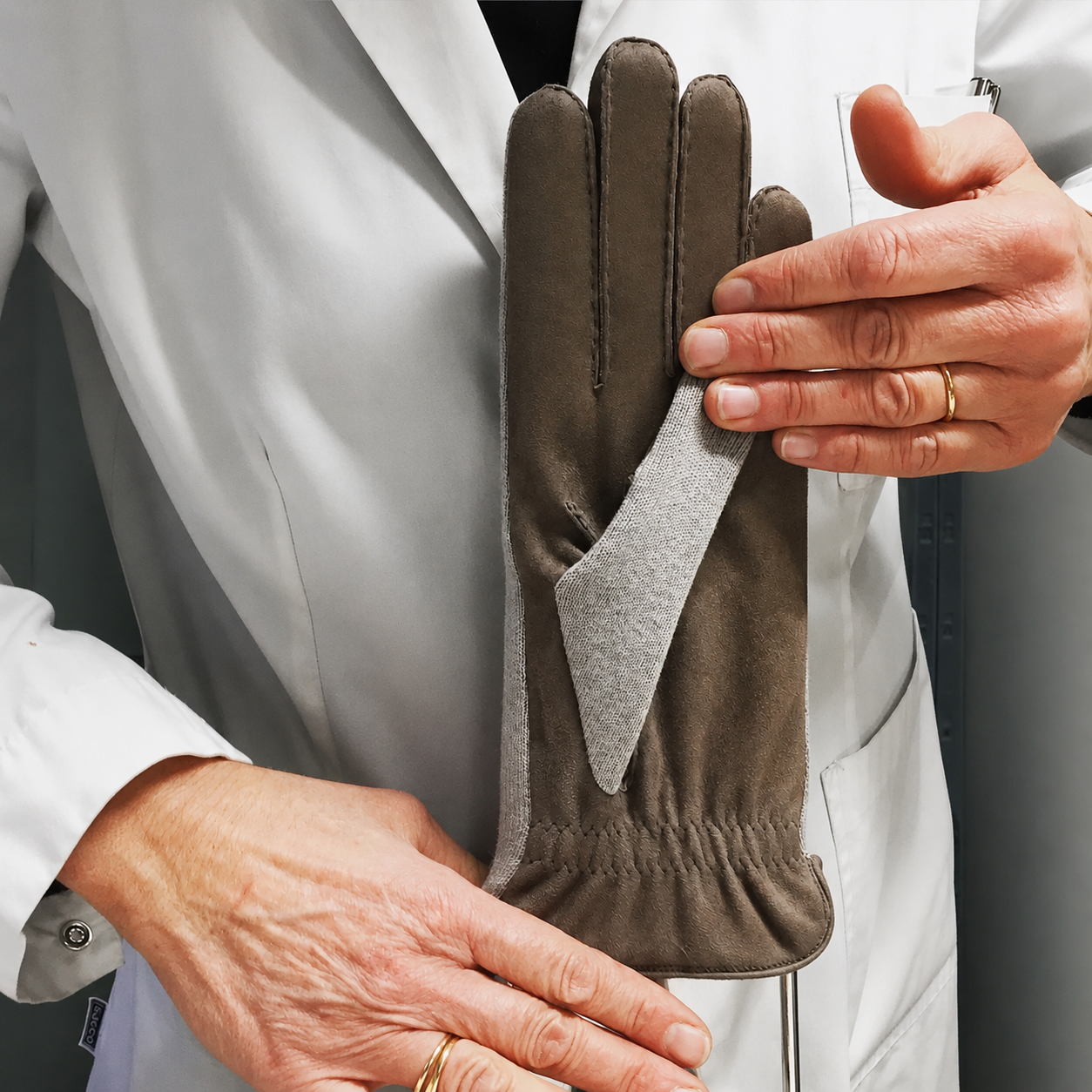 Une personne tenant une paire de gants en cuir marron, portant une veste blanche, dans un environnement professionnel.