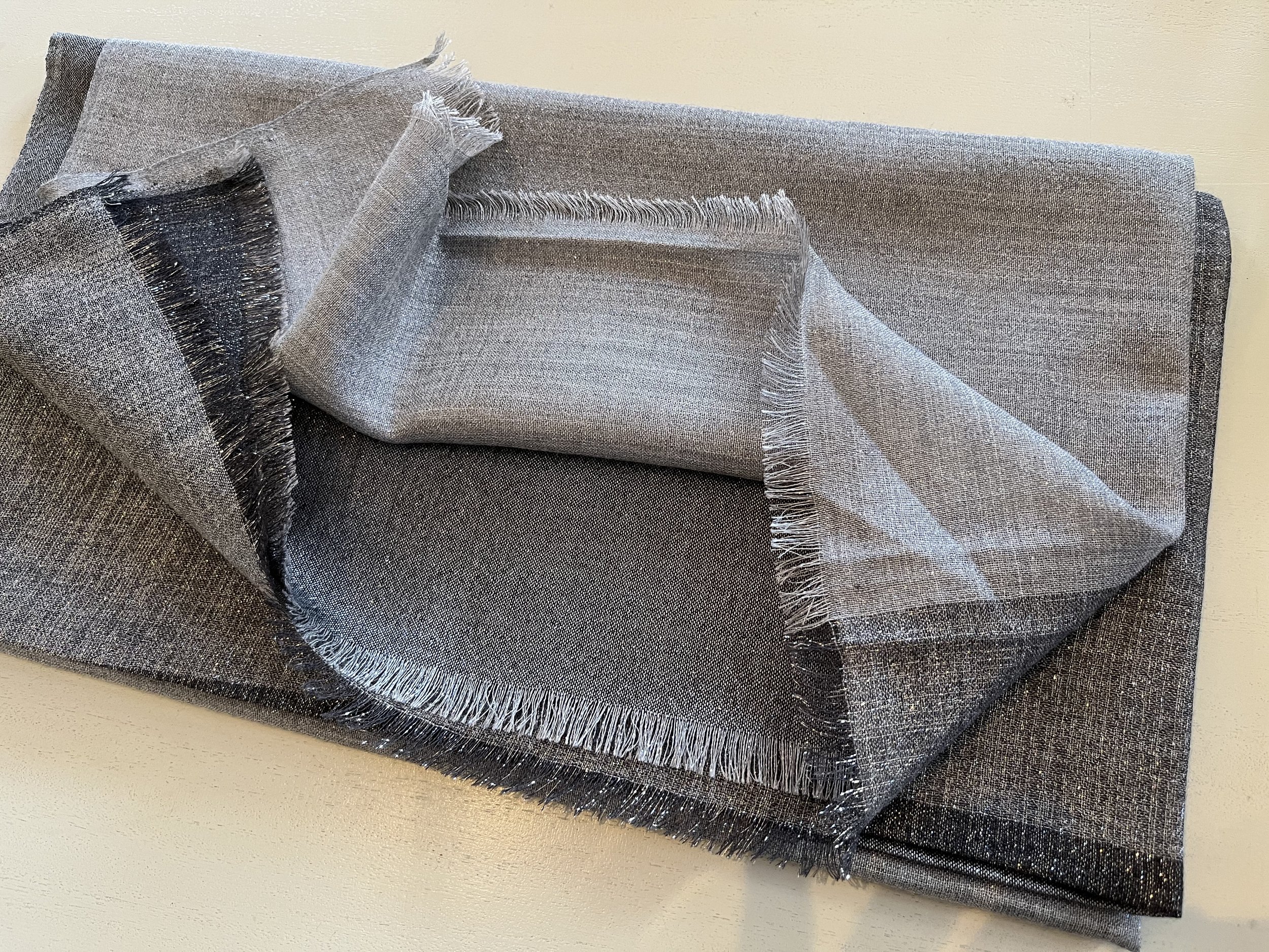 Écharpe en tissu gris à franges, pliée et posée sur une surface