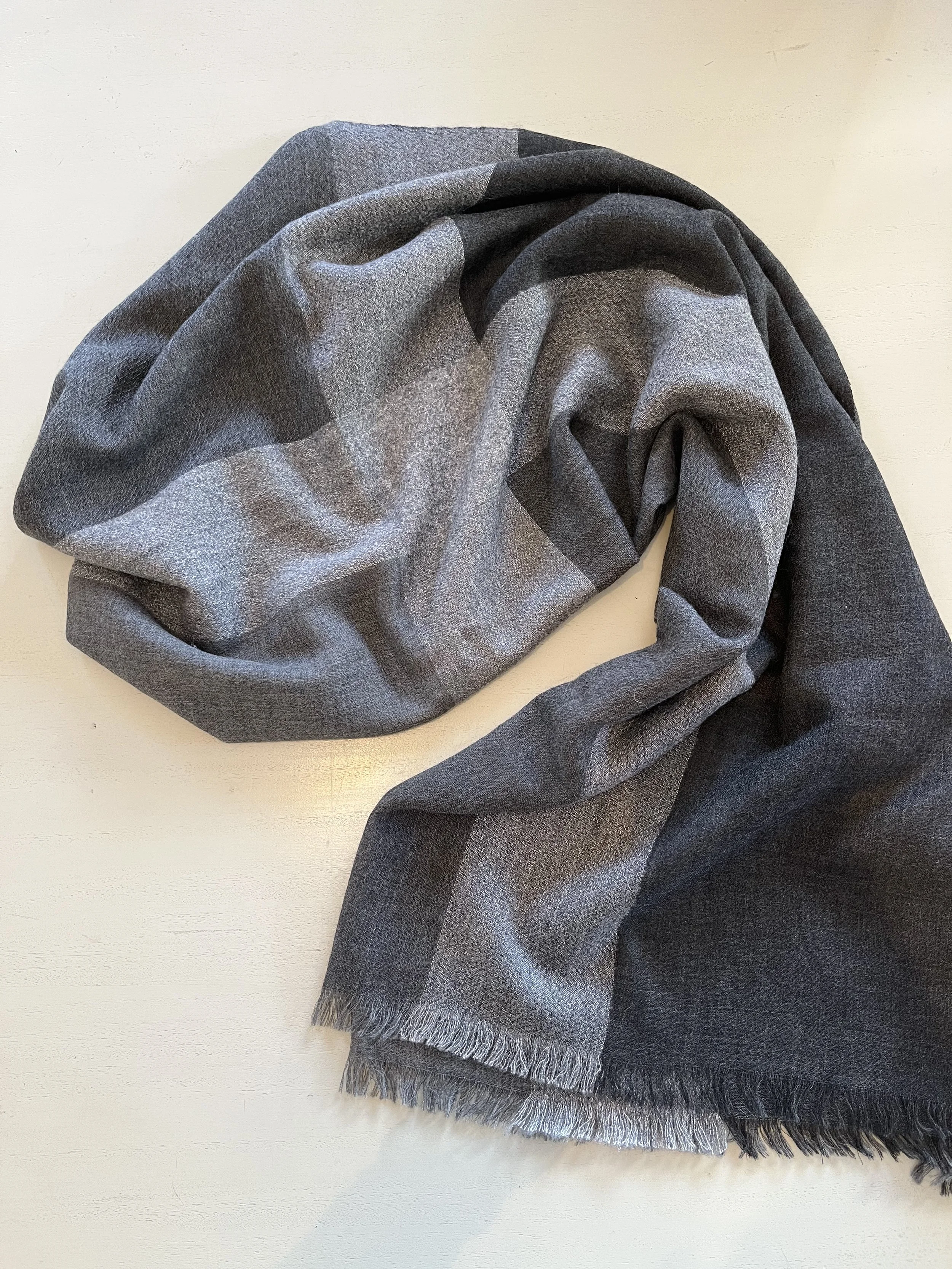 Un foulard en laine gris, plié et posé sur une surface blanche.