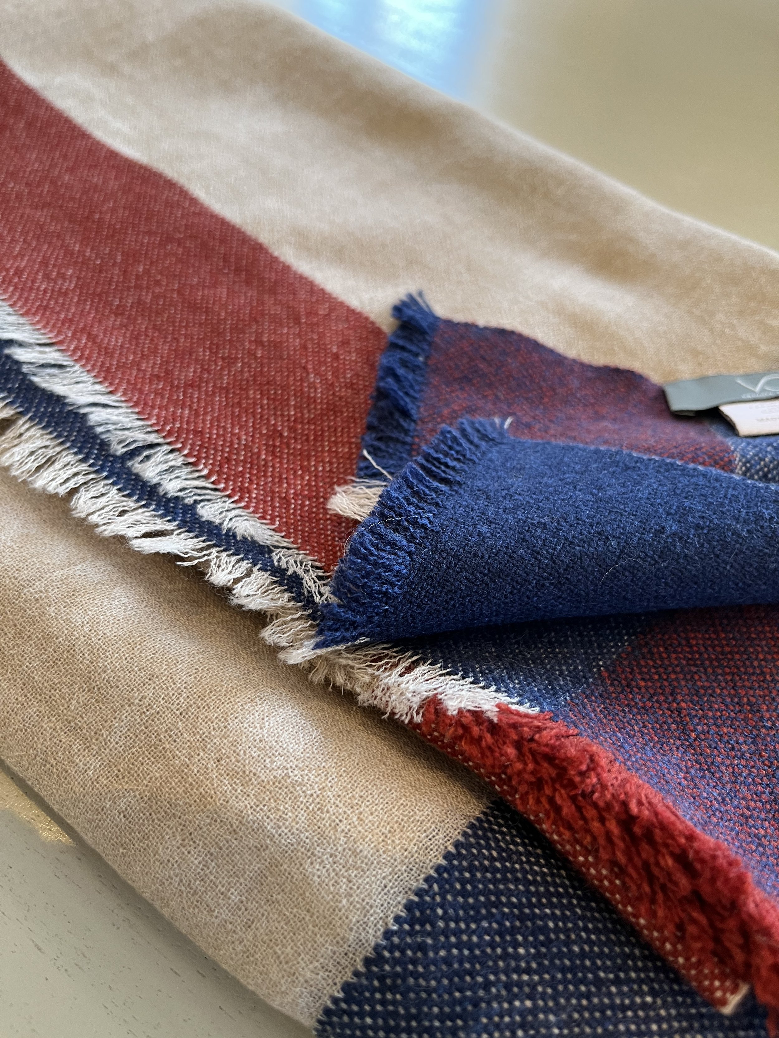 Echarpe en laine aux couleurs rouge, beige, bleu et détails à franges, posée sur une surface