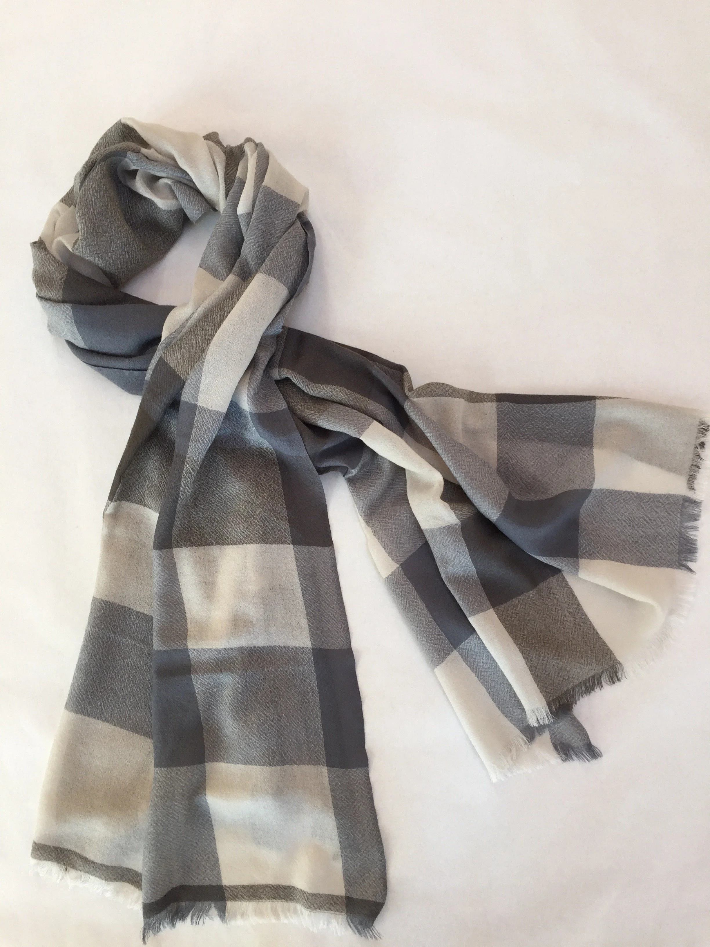 Un foulard à carreaux gris, blanc et noir posé sur un fond blanc.