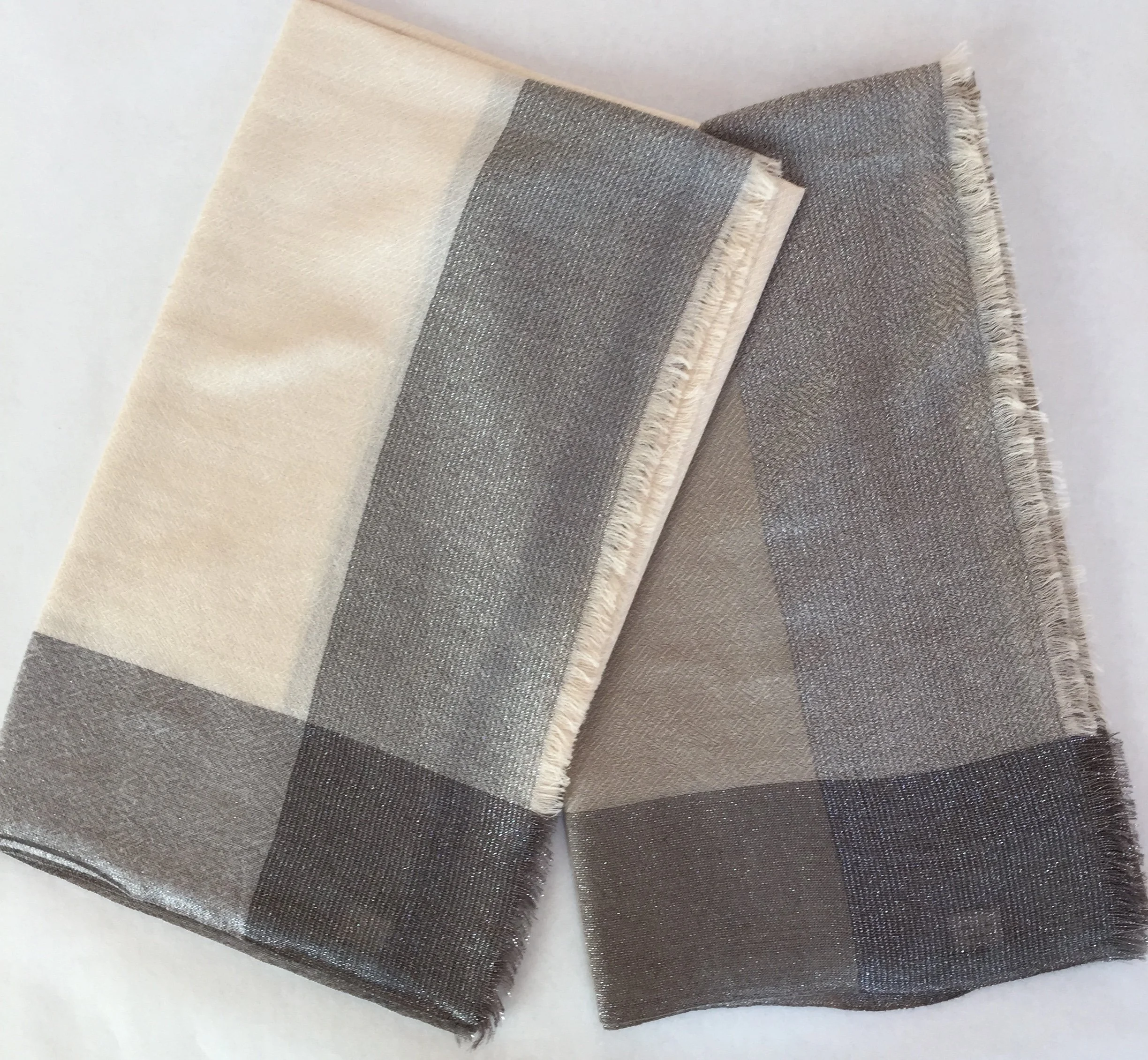 Trois carrés de tissu en matières brillantes et en couleurs neutres, disposés en décalé avec des bords frangés, sur un fond blanc.