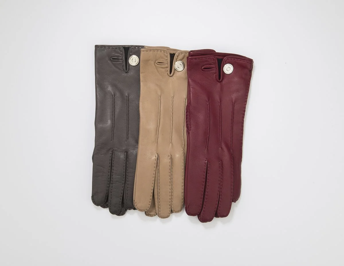 Trois paires de gants en cuir de différentes couleurs : noir, beige et rouge, posés côte à côte sur un fond blanc.