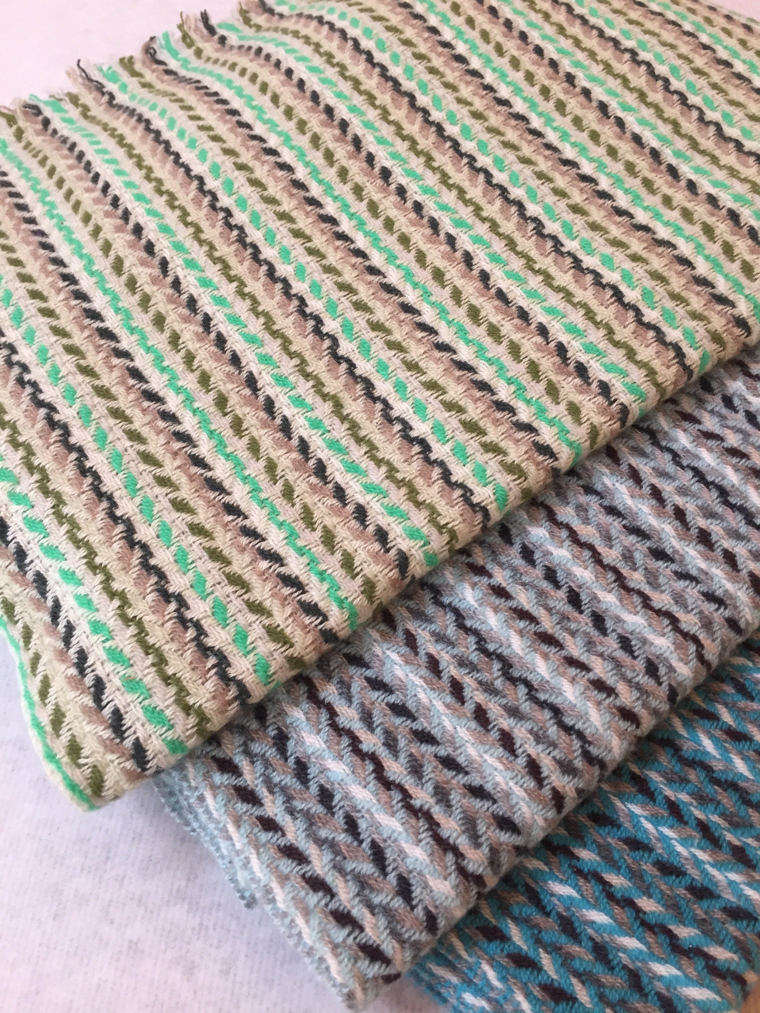 Trois rouets de laine à torsader en différentes couleurs : vert, beige, gris et bleu, disposés sur une surface blanche.
