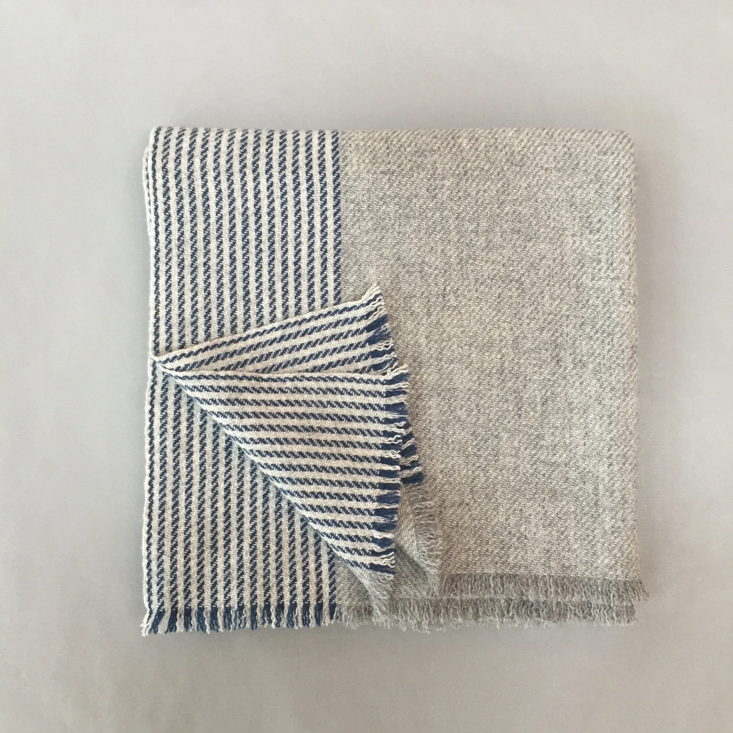 Un tissu léger avec rayures bleues et blanches et un autre tissu beige ou taupe sans motif, tous deux pliés. Téléphone blanc dans le coin supérieur gauche.