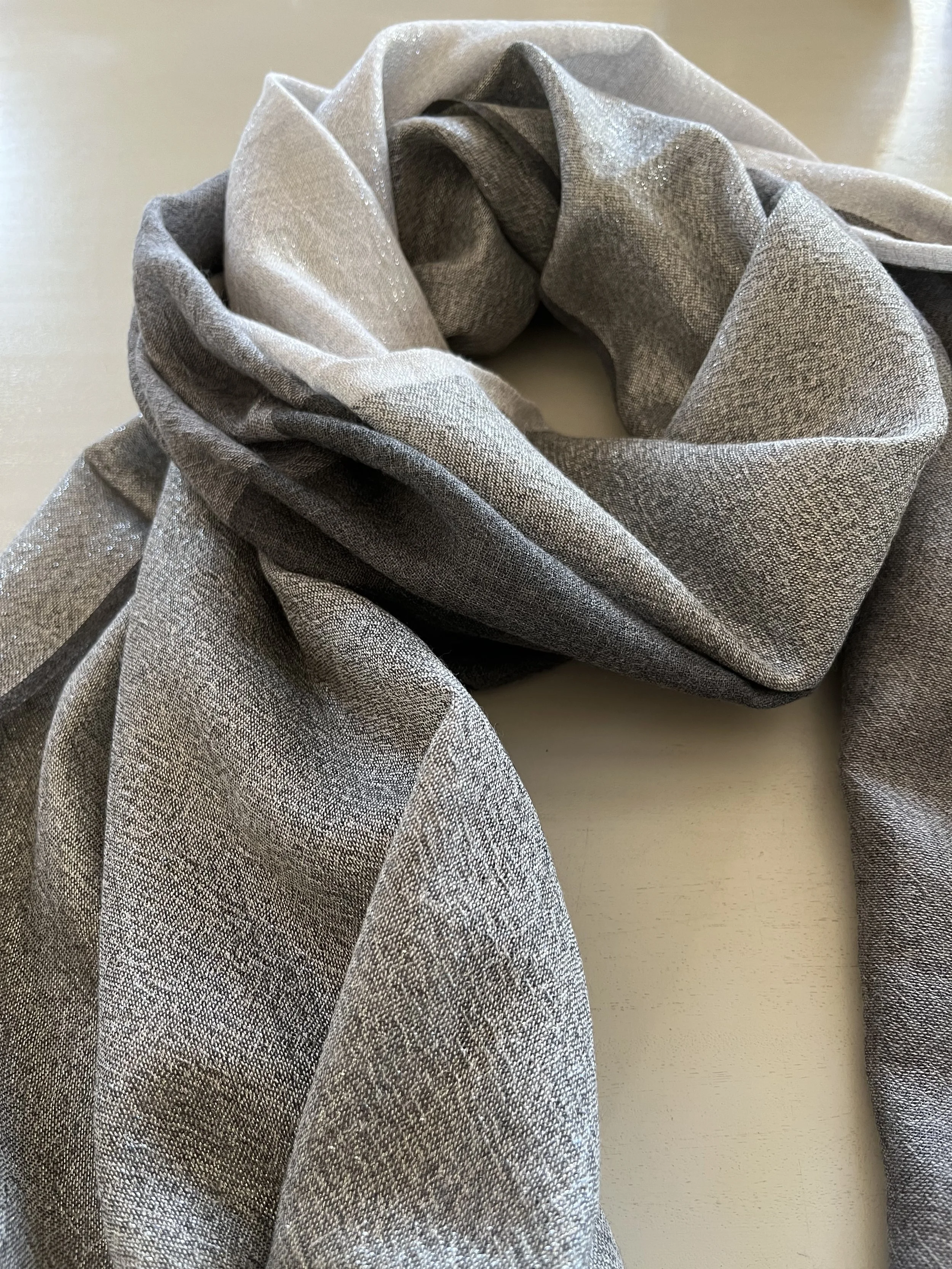 Un foulard en tissu gris clair, avec un motif en tissage fin, posé sur une surface claire.