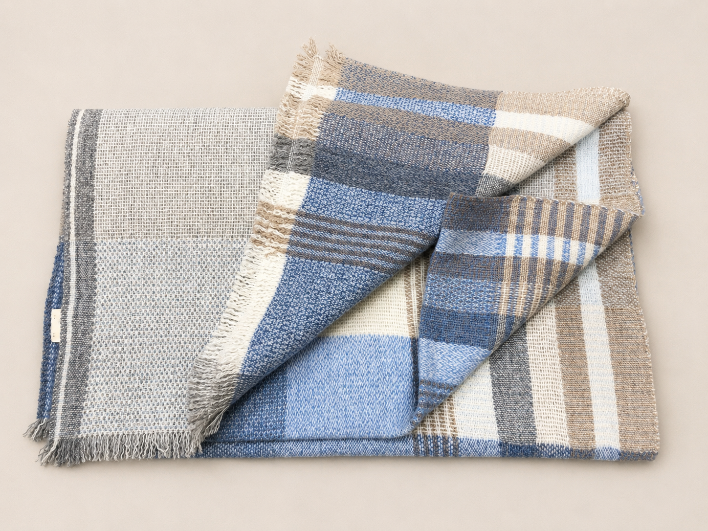 Deux nappes ou serviettes en tissu à motifs à carreaux beige, bleu, blanc et gris, disposées l'une sur l'autre sur une surface claire.