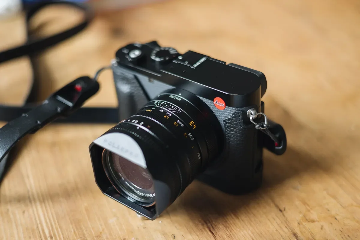 A black Leica Q3 43 with a neck strap, resting on a wooden surface.