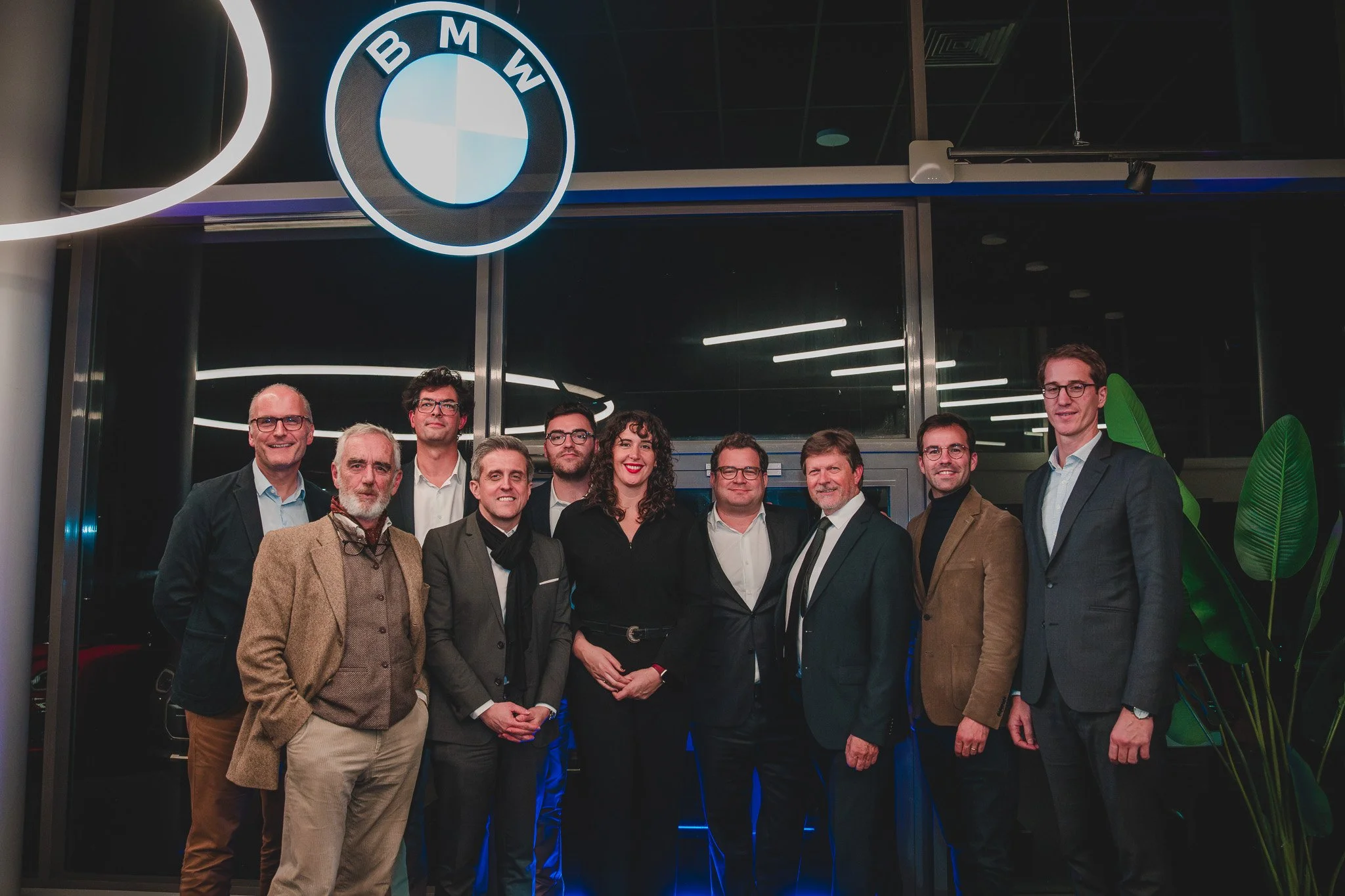 Groupe de personnes en costume dans un showroom BMW, avec le logo BMW en éclairage au plafond.