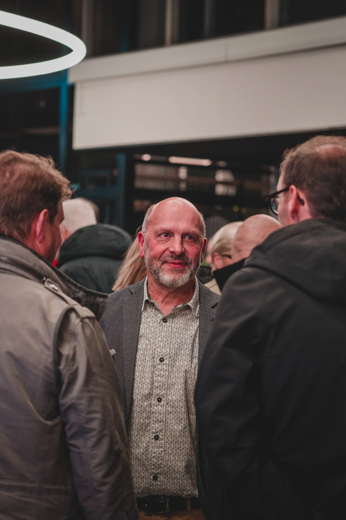 Un homme au centre souriant, entouré de plusieurs autres personnes, semble en conversation lors d'un événement ou d'une rencontre.