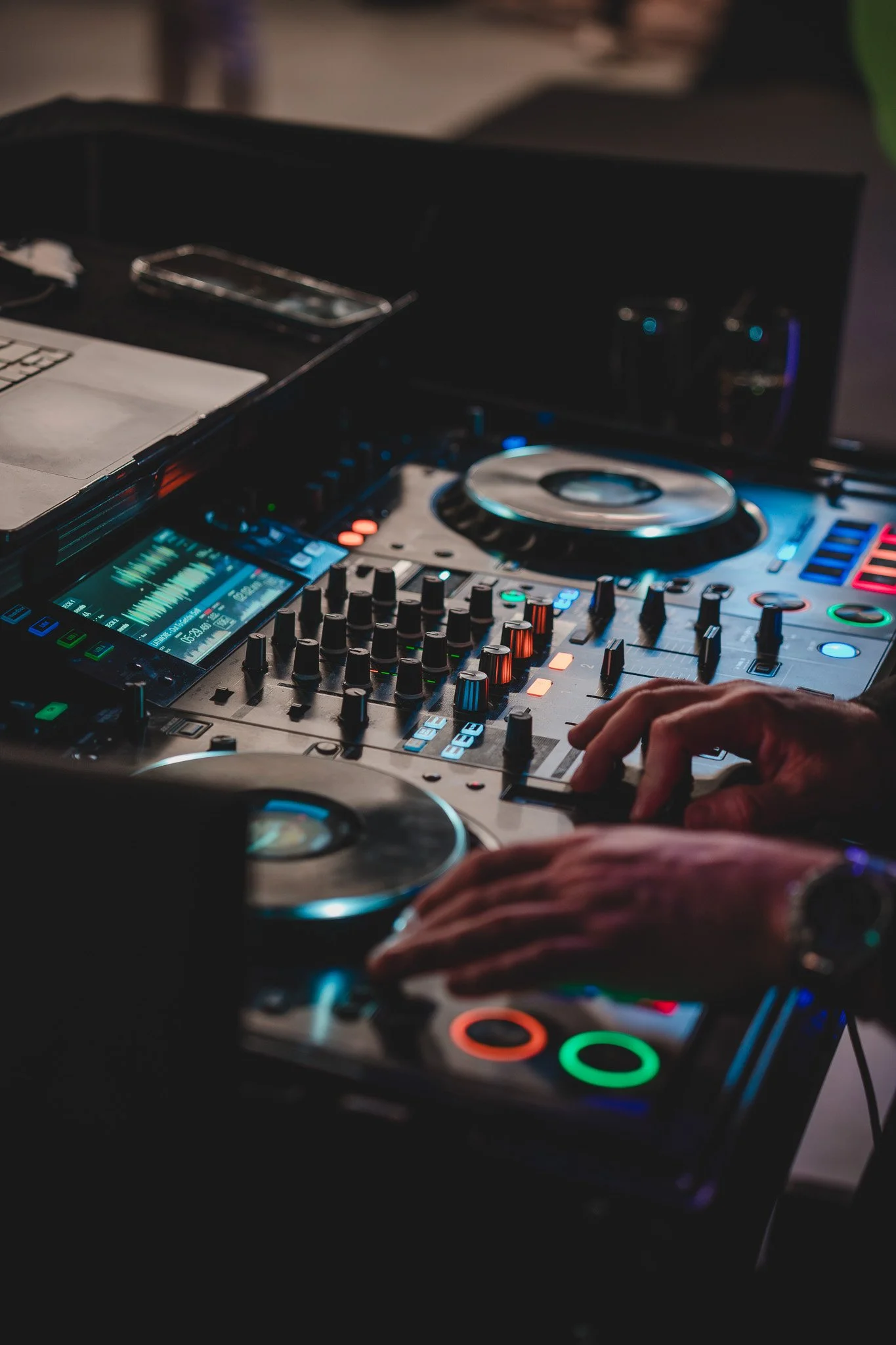 Un DJ en train de mixer avec un équipement électronique coloré et éclairé, en utilisant ses mains.